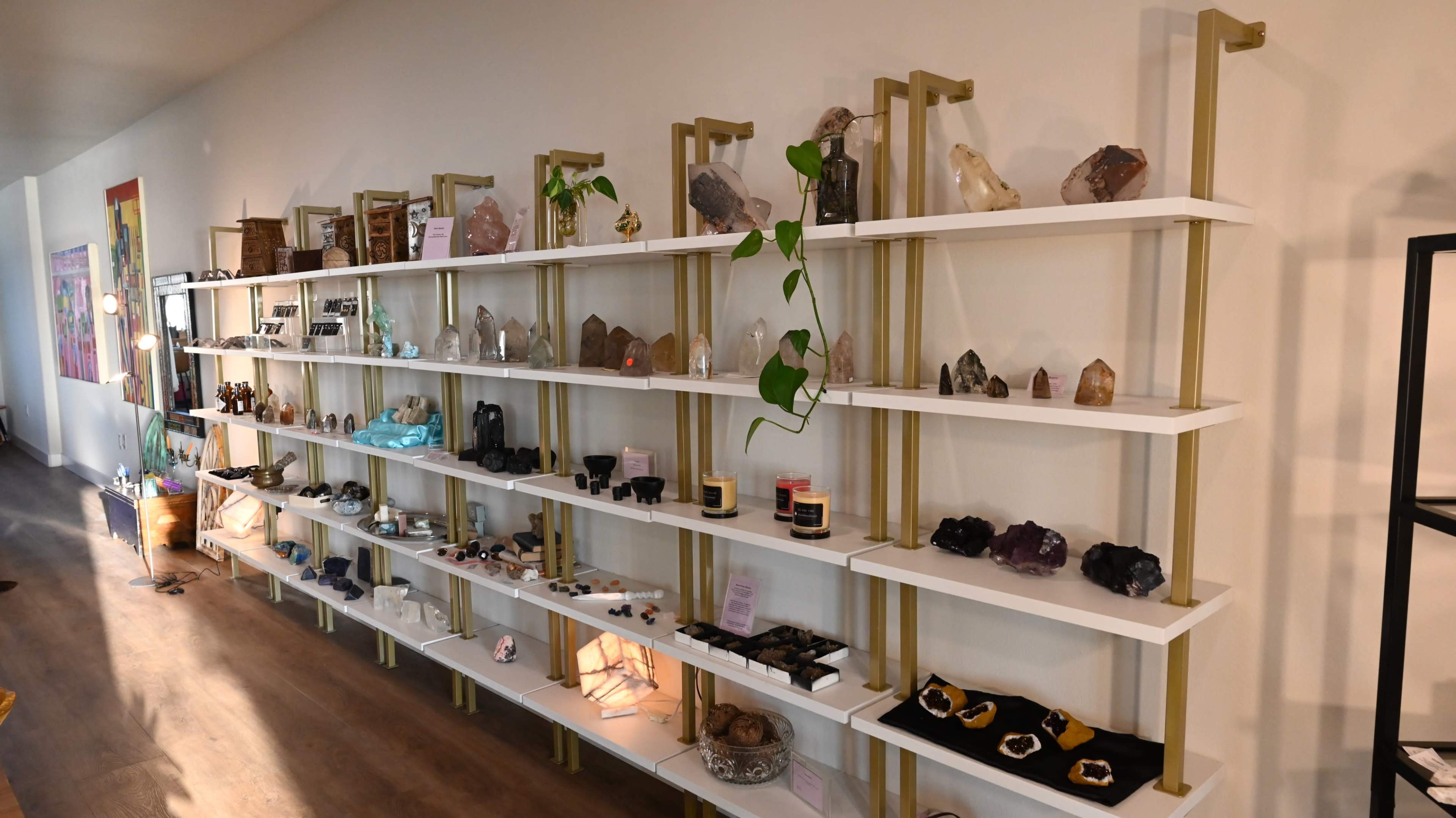 A display of various crystals and decorative items arranged on white shelves against a plain wall.