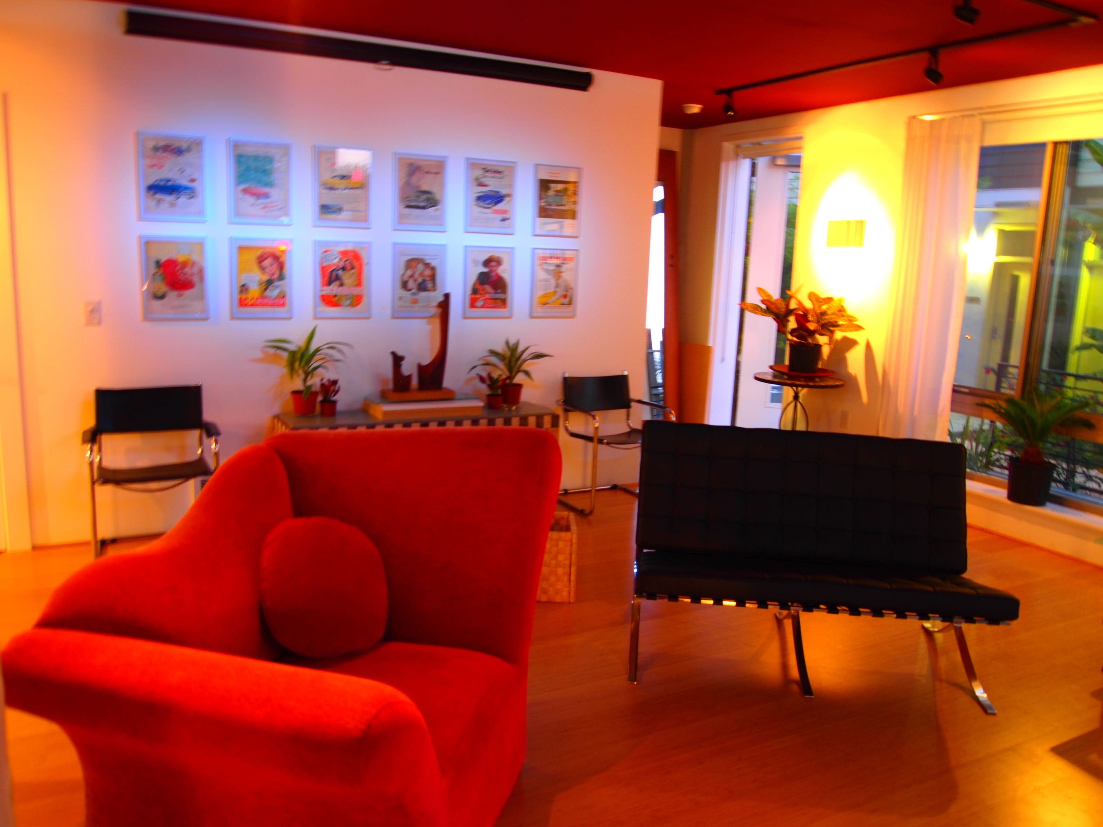 A modern interior space featuring red furniture, artwork on the wall, and plants beside large windows.