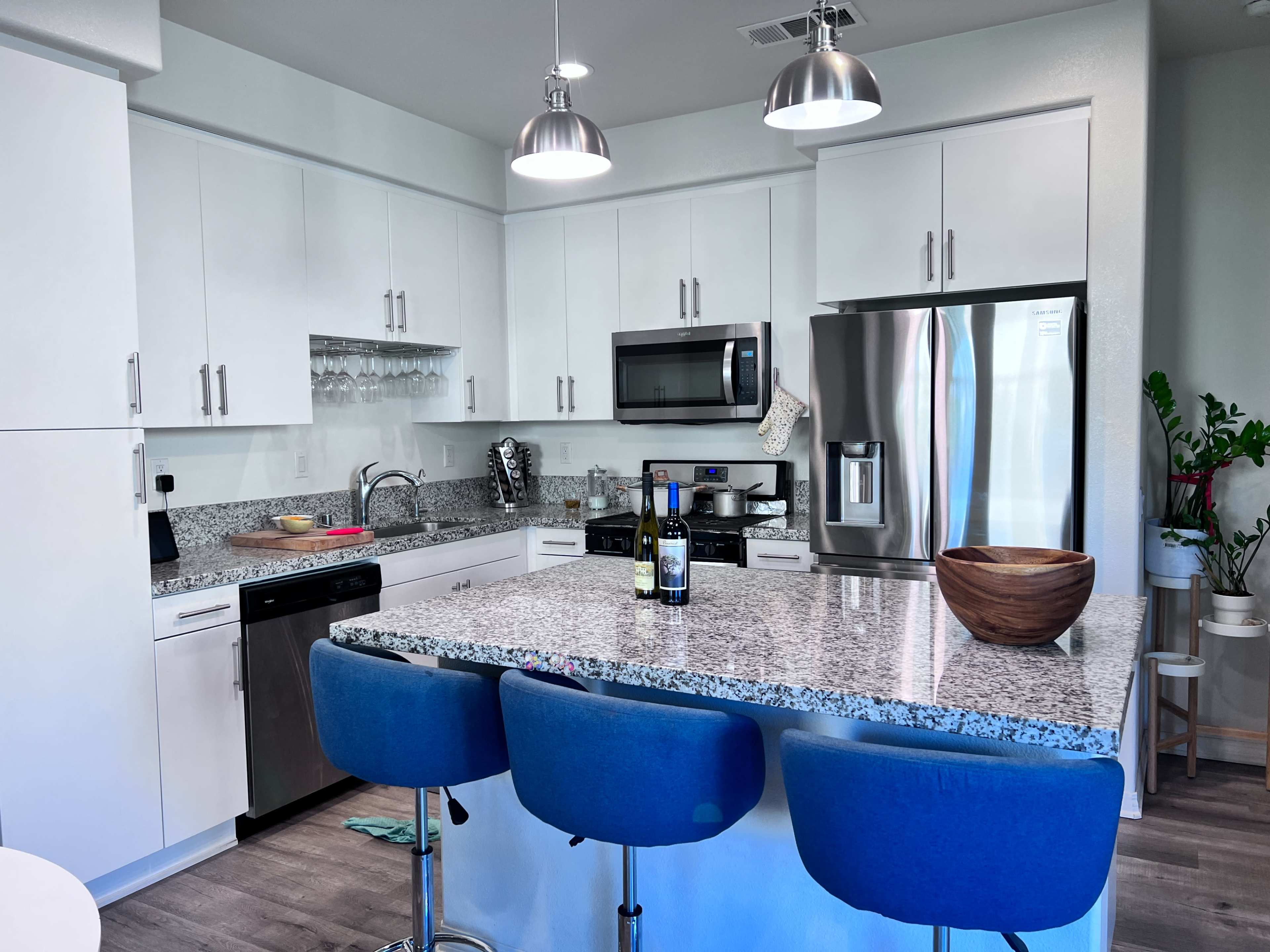 A modern kitchen with white cabinets, stainless steel appliances, a granite countertop, and blue bar stools.