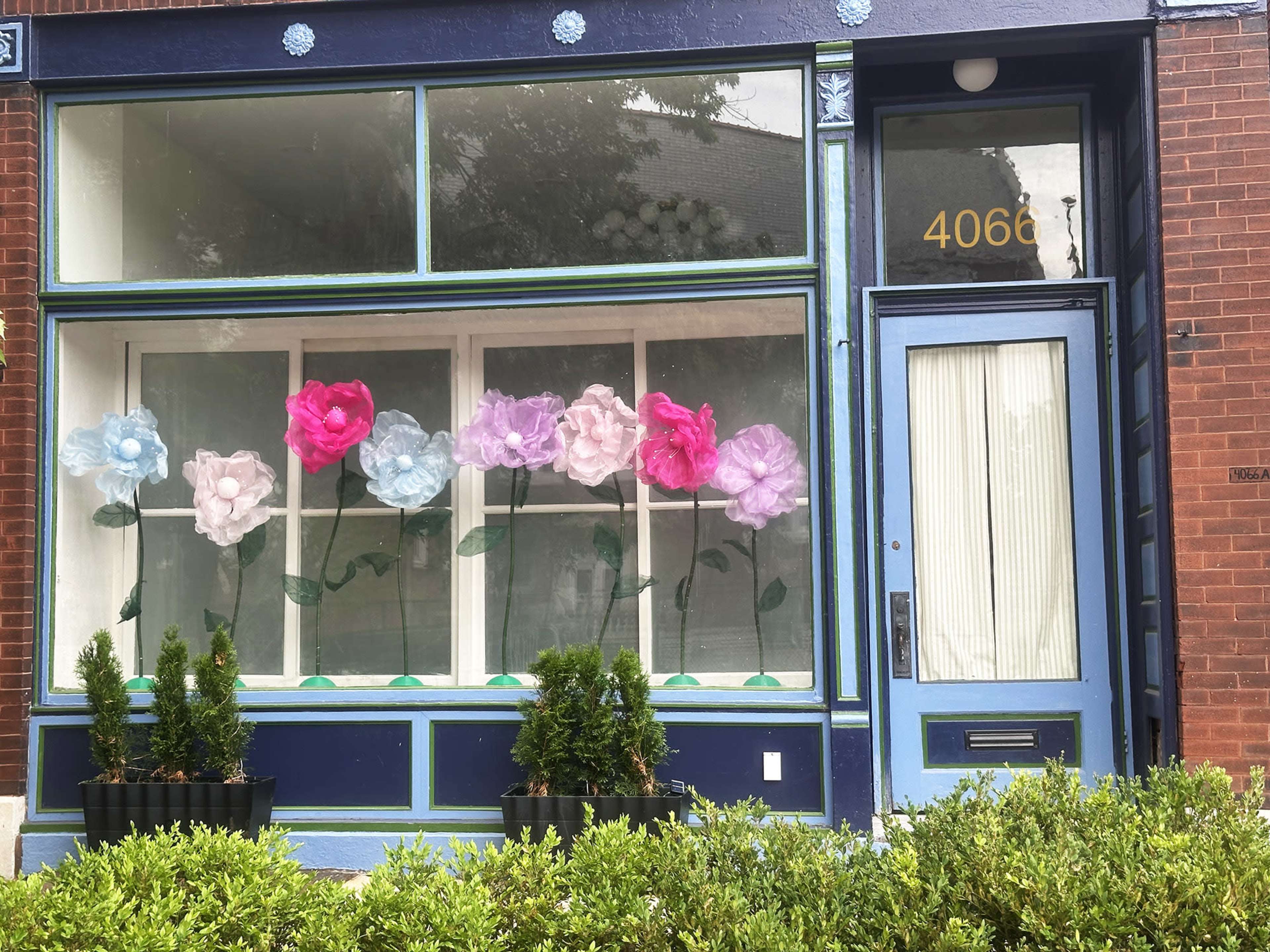 The storefront features large, colorful artificial flowers displayed in the windows alongside small potted plants.