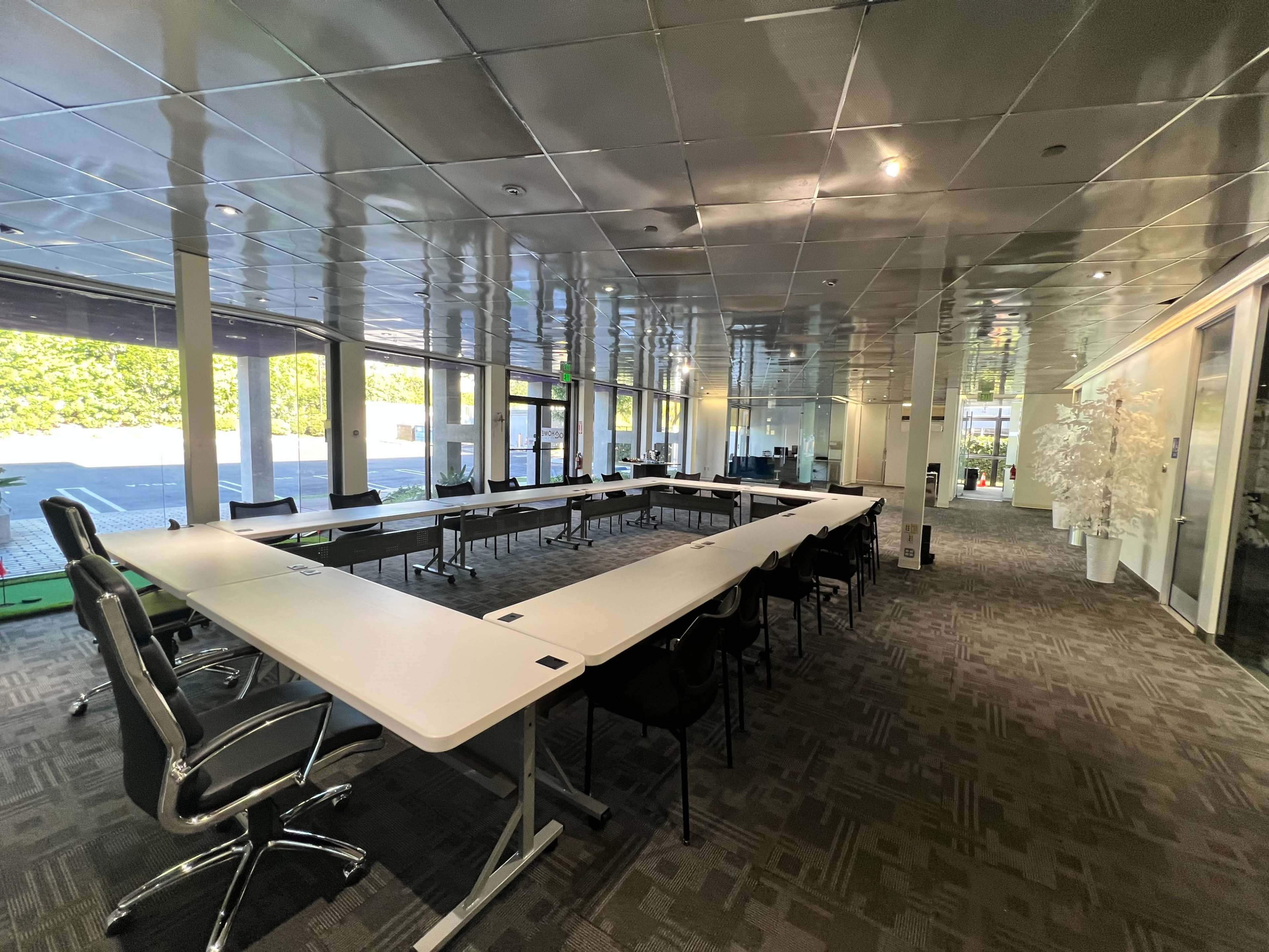 A modern conference room features a large, rectangular table surrounded by chairs and has glass walls overlooking an outdoor area.