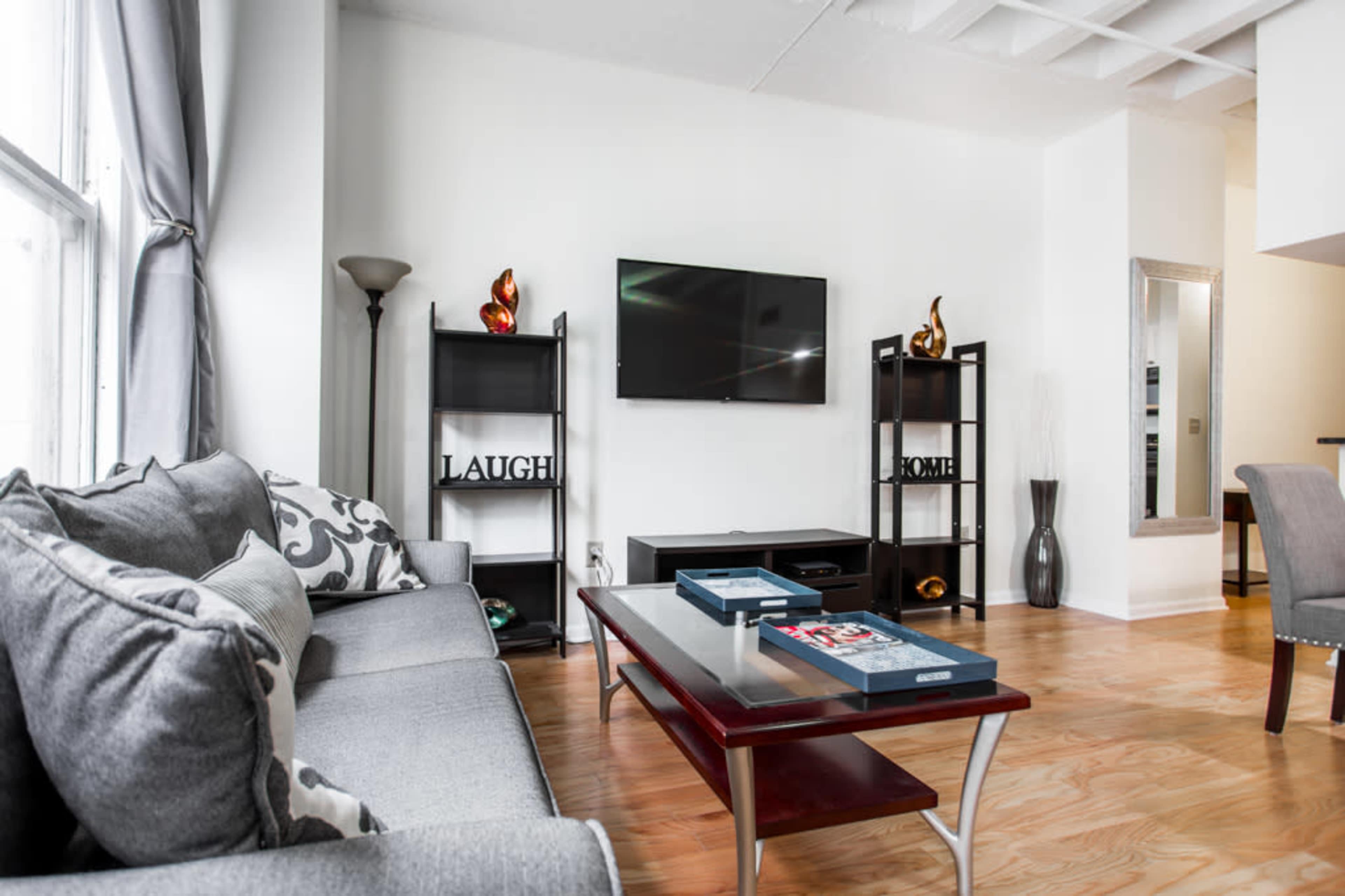 A modern living room with a gray sofa, a coffee table, a television mounted on the wall, and shelves on either side displaying decorative items.