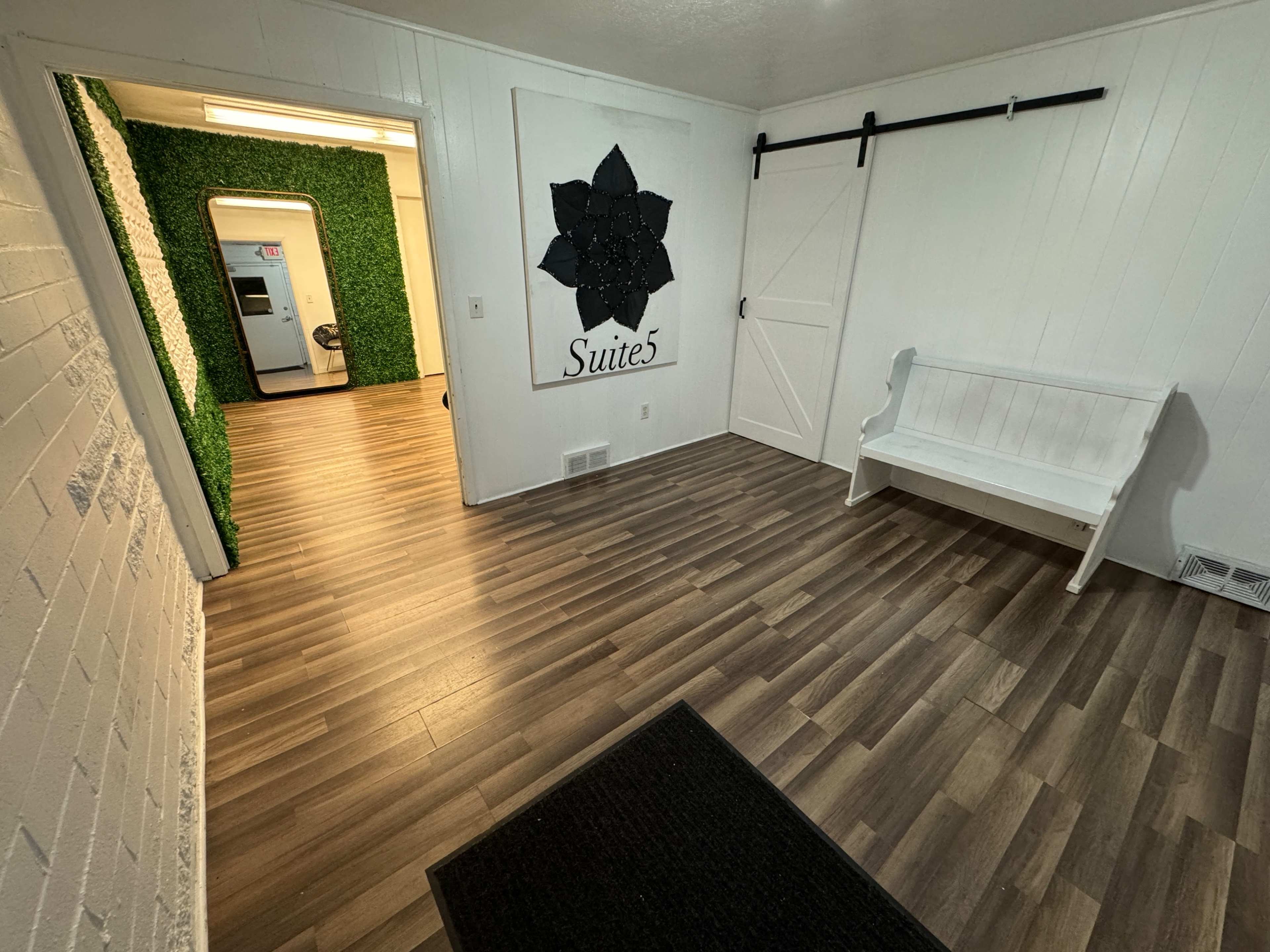 A small waiting area with wooden flooring, a white bench, and a decorative wall featuring a black flower design with the label "Suite 5."