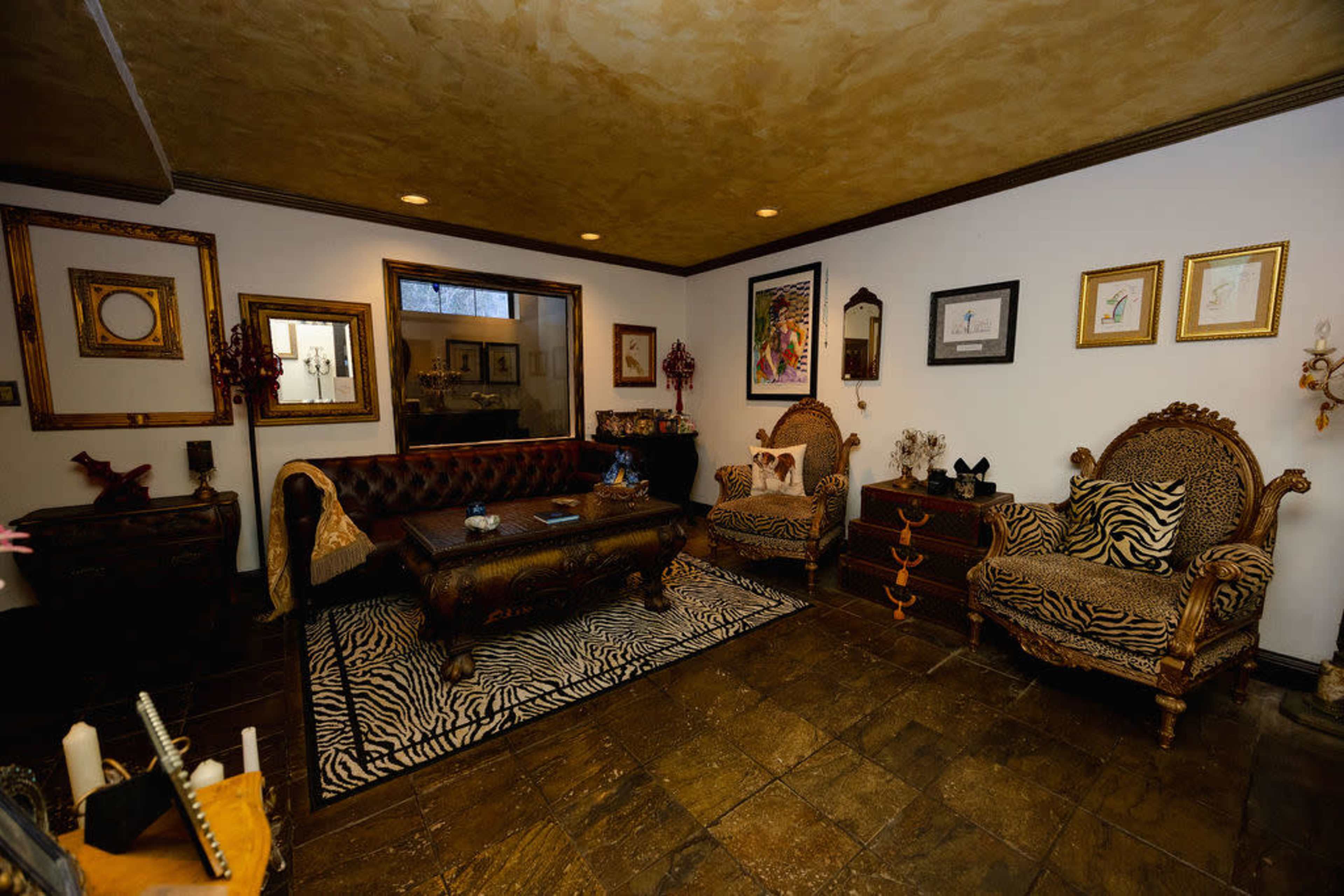 The image shows a living room with ornate furniture, including a patterned sofa and armchairs, accented by zebra-striped decor on the rug.