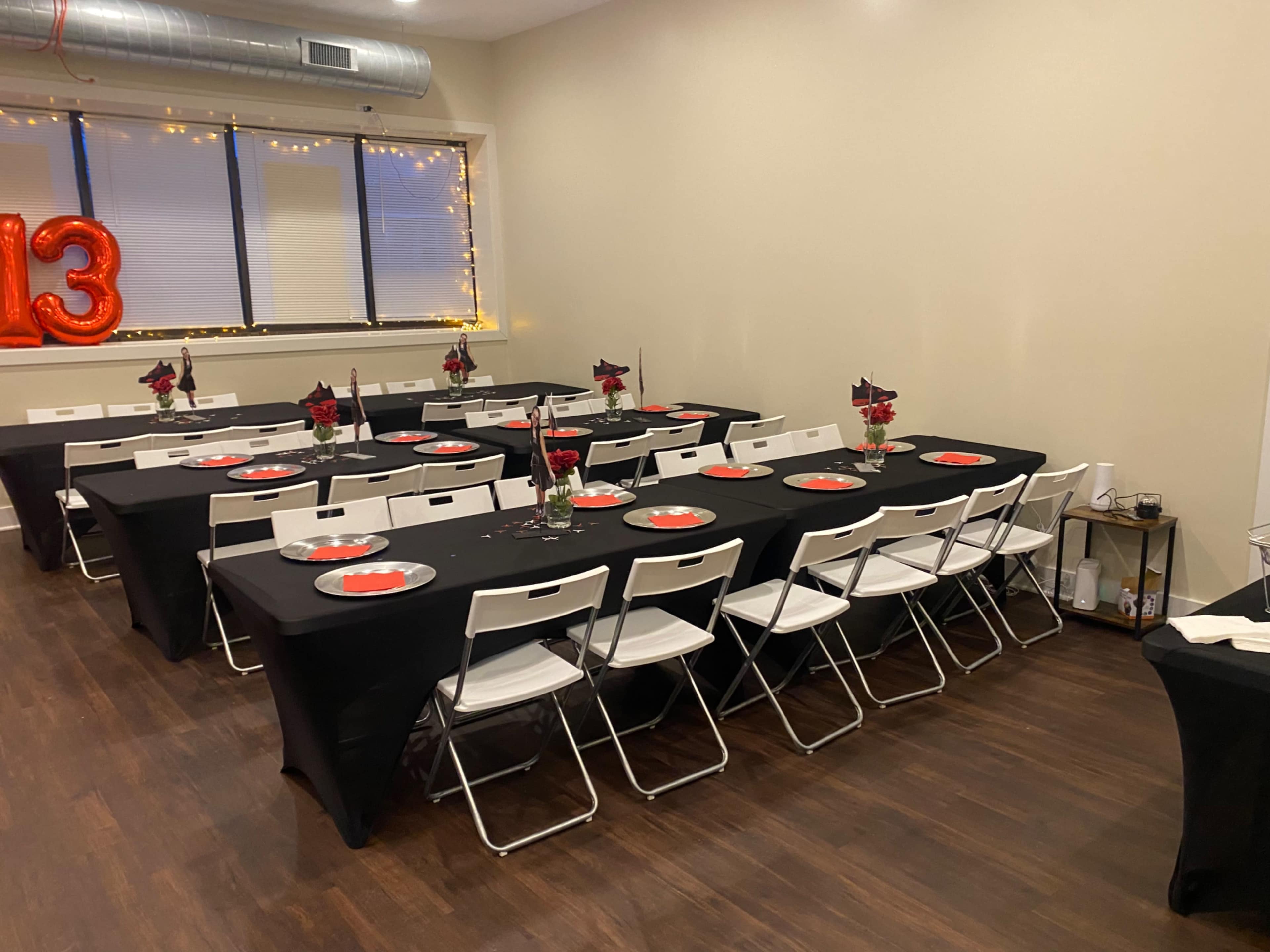 A decorated event space features rows of tables covered with black tablecloths, each set with red plates and floral centerpieces.