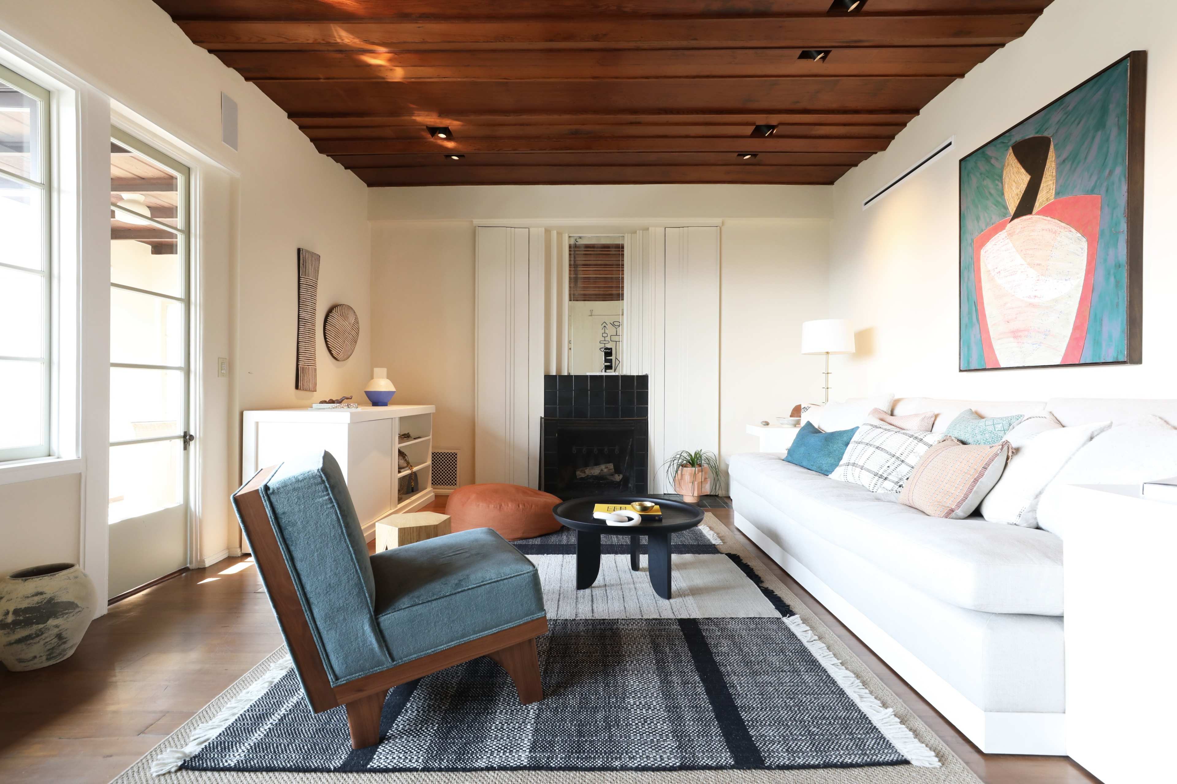 A modern living room with a white sofa, a wooden ceiling, and a large abstract painting on the wall.