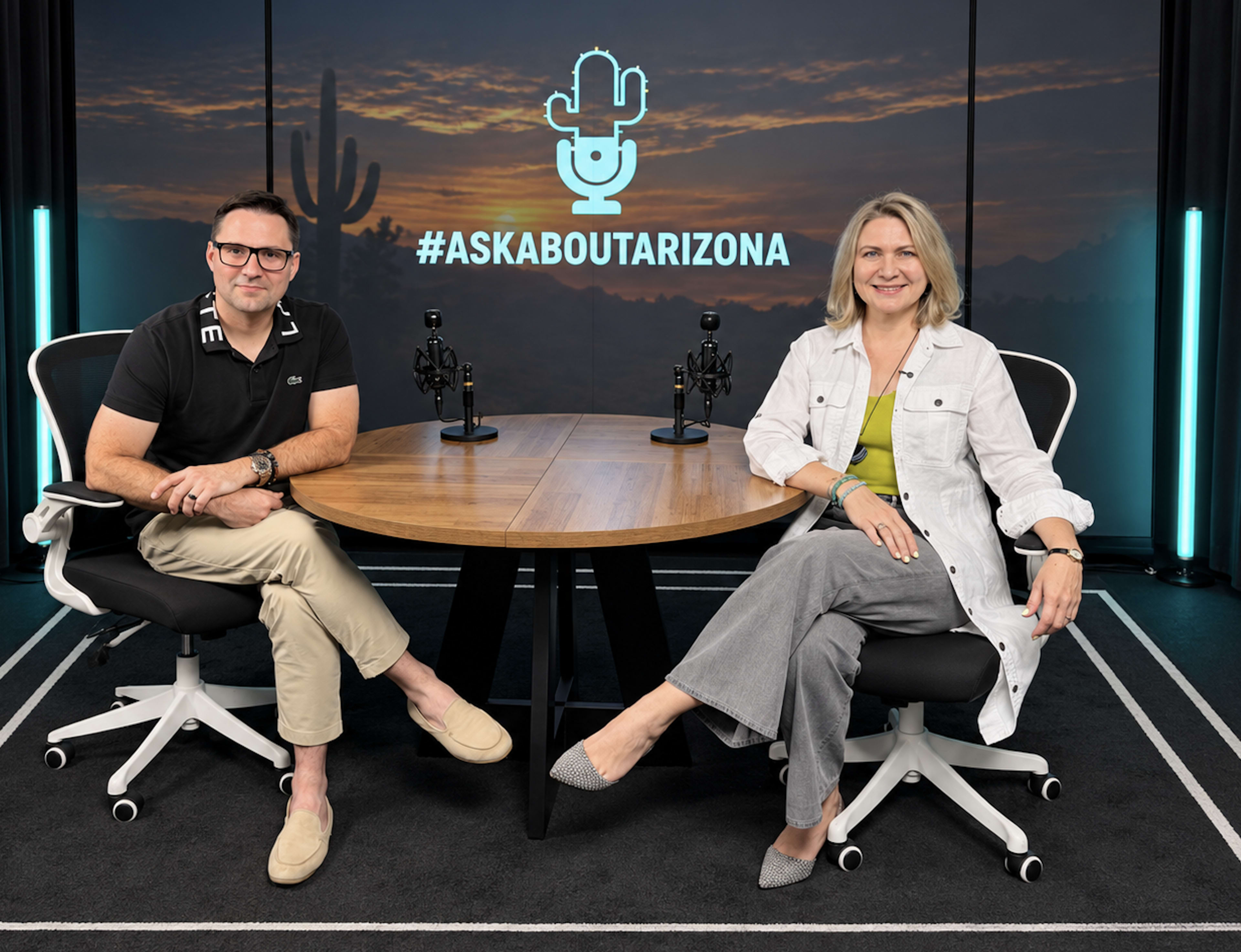 Two people are seated at a wooden table in a studio with a backdrop featuring a desert landscape, microphones set up around them, and the hashtag "#ASKABOUTARIZONA" displayed centrally.