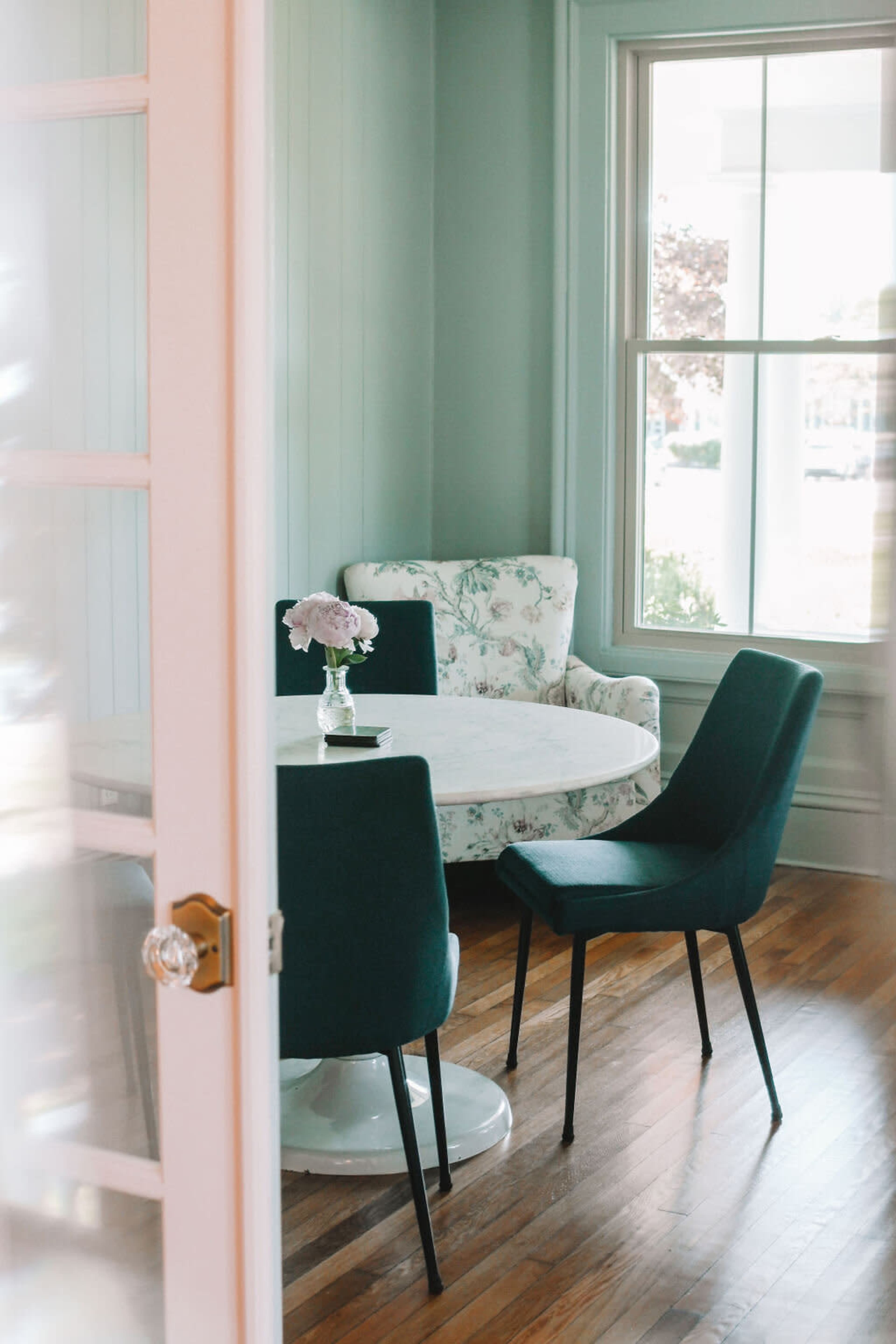 A small dining area features a round table surrounded by three chairs and a floral couch next to a large window.
