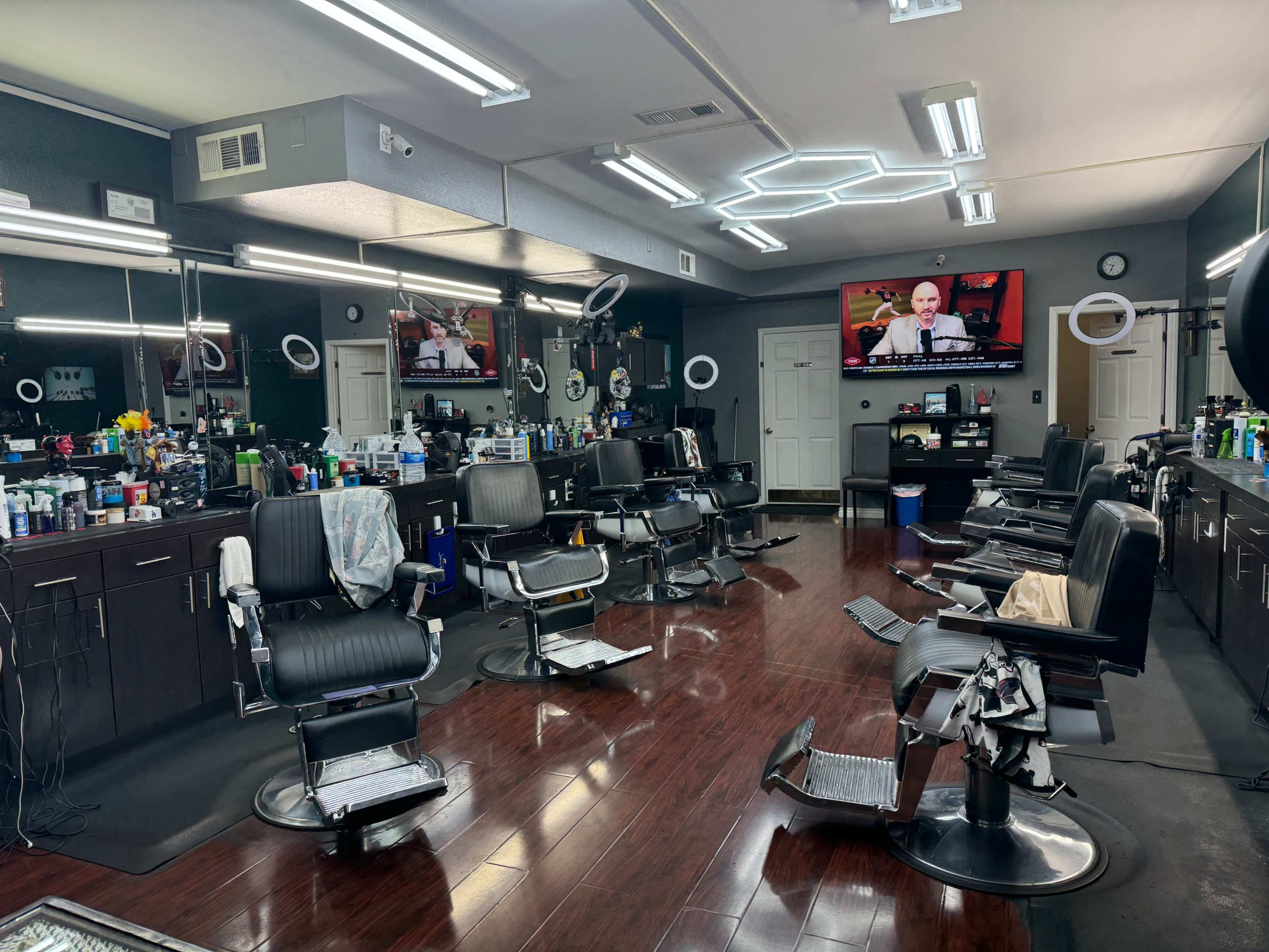 The image shows a barbershop interior featuring several empty barber chairs, mirrors, and a television mounted on the wall.