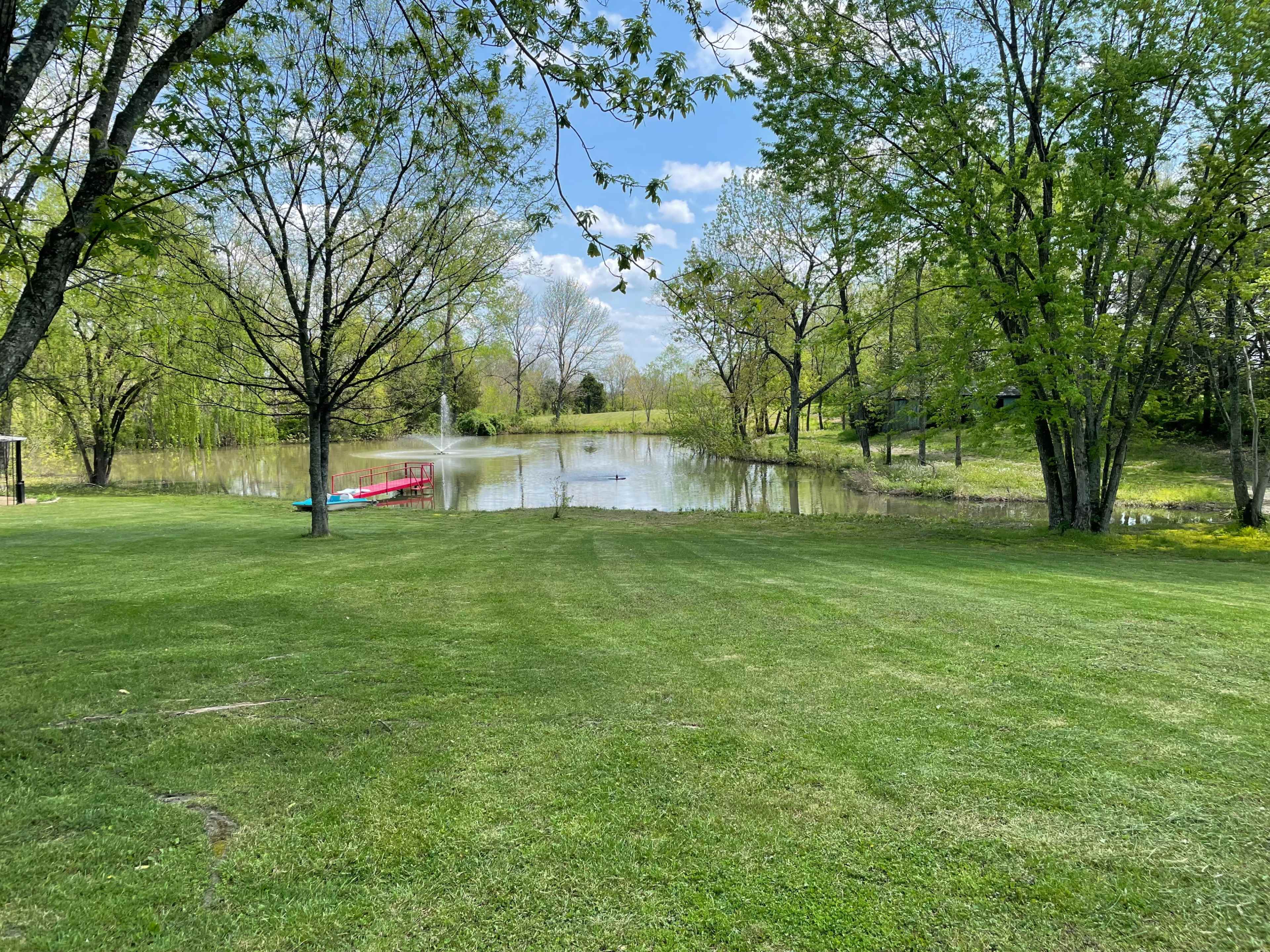 A serene pond surrounded by lush greenery and trees, with a small red canoe on the water's edge.