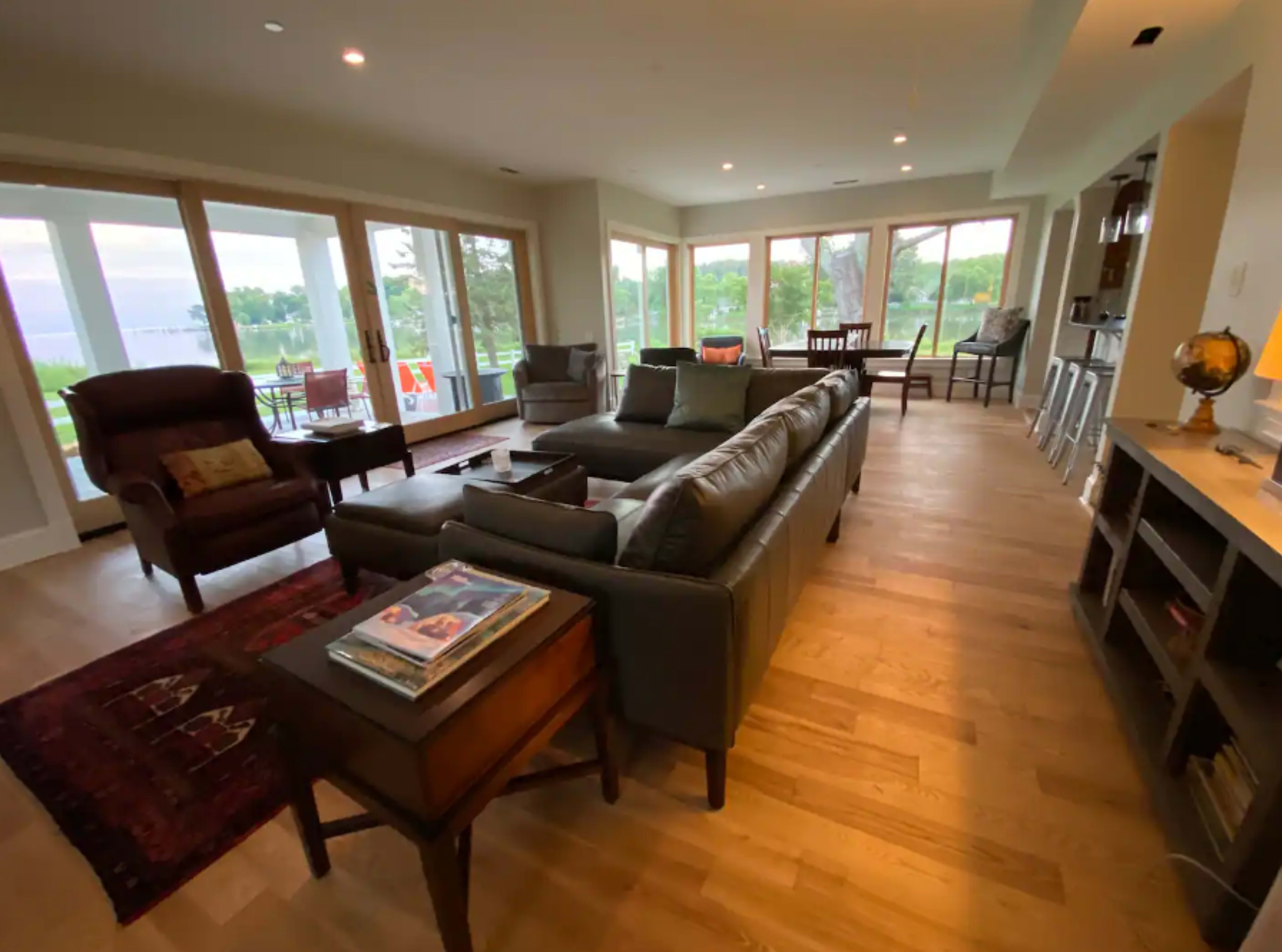 The living room features large windows overlooking a picturesque landscape, with modern furniture arranged around a central seating area.