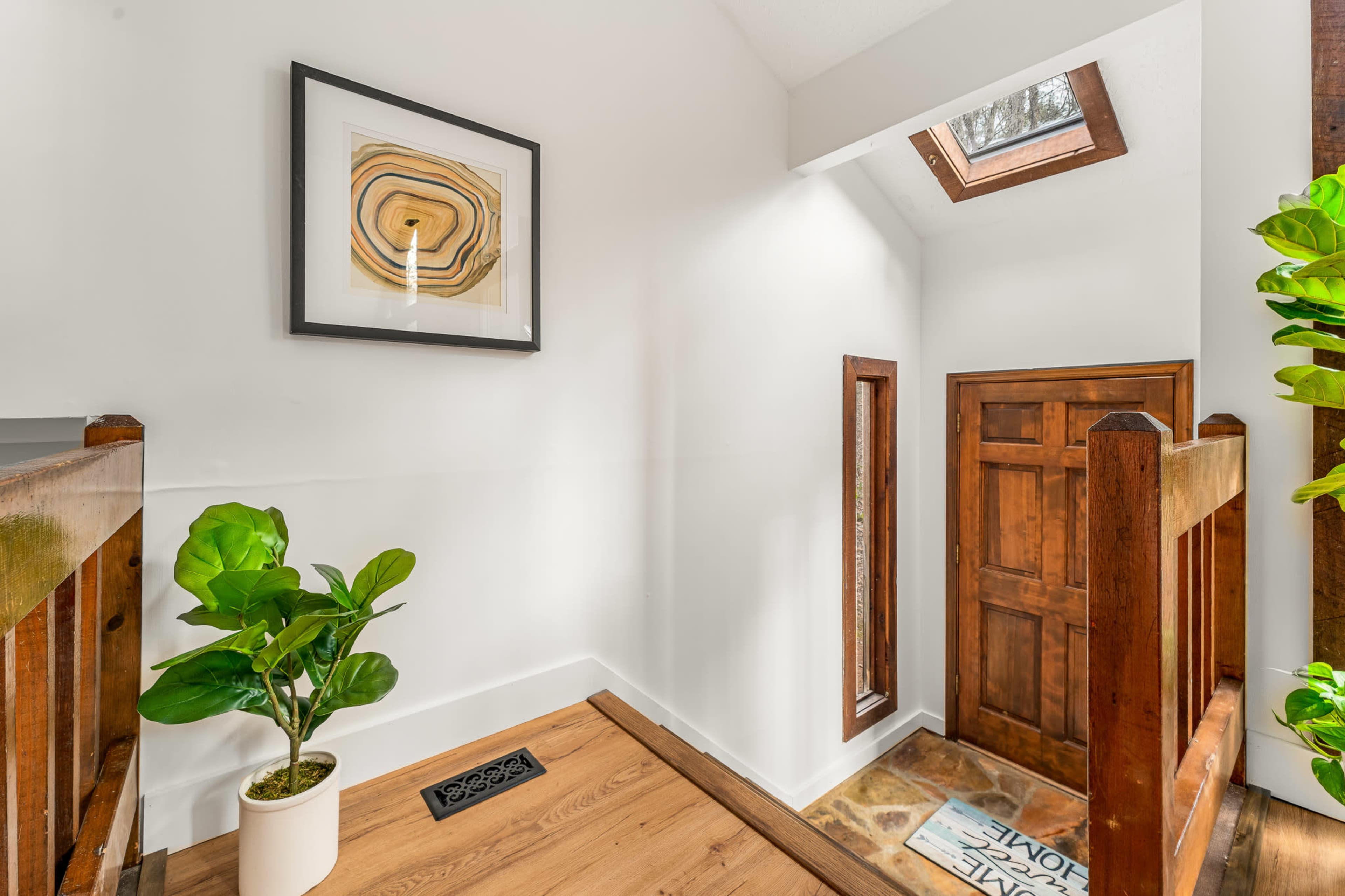The image shows a well-lit staircase landing with a wooden door, a potted plant, and a skylight overhead.