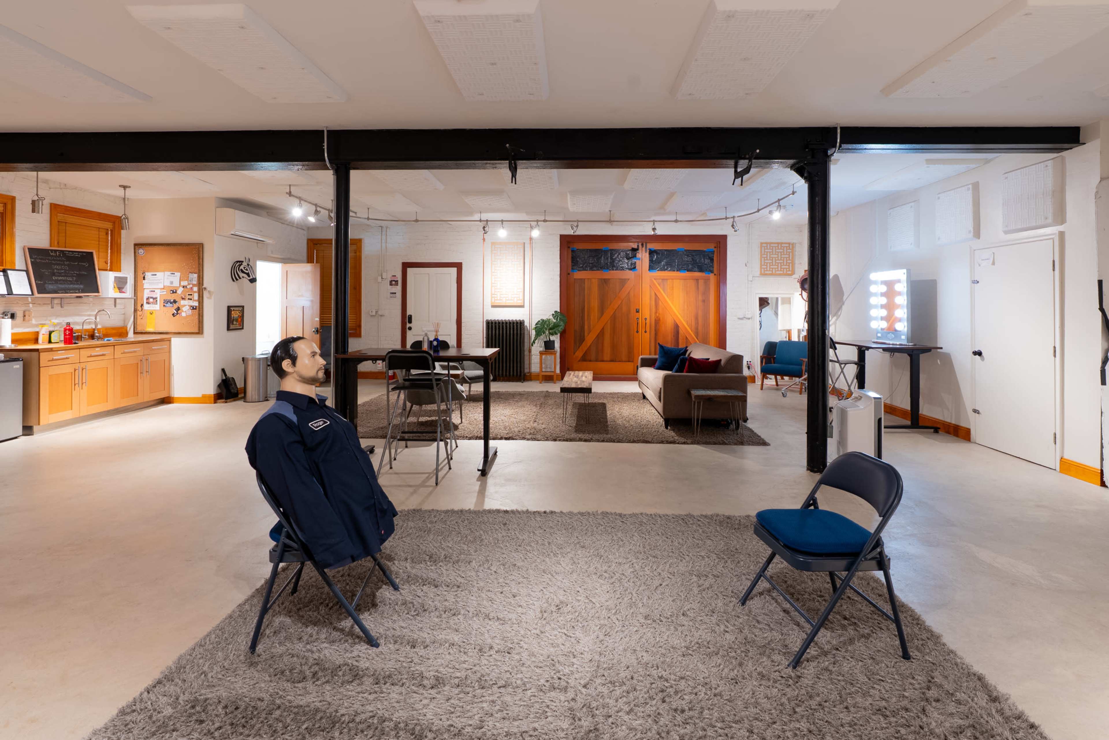 The image shows an open, modern living space featuring a kitchen area, a sitting area with a sofa, and two blue chairs positioned on a gray rug facing each other.