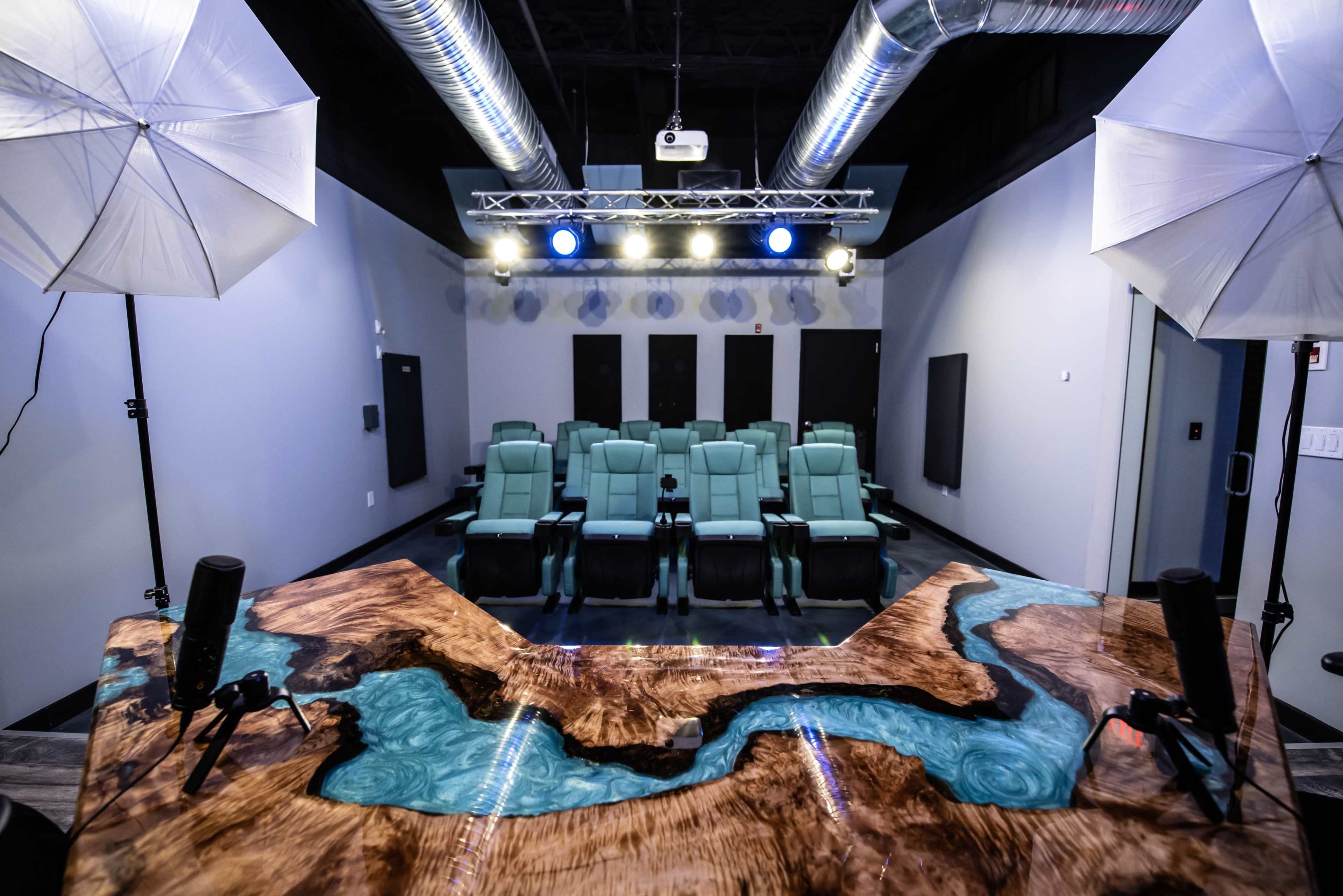 A modern home theater setup with green reclining seats facing a projector screen, and professional lighting equipment positioned above.