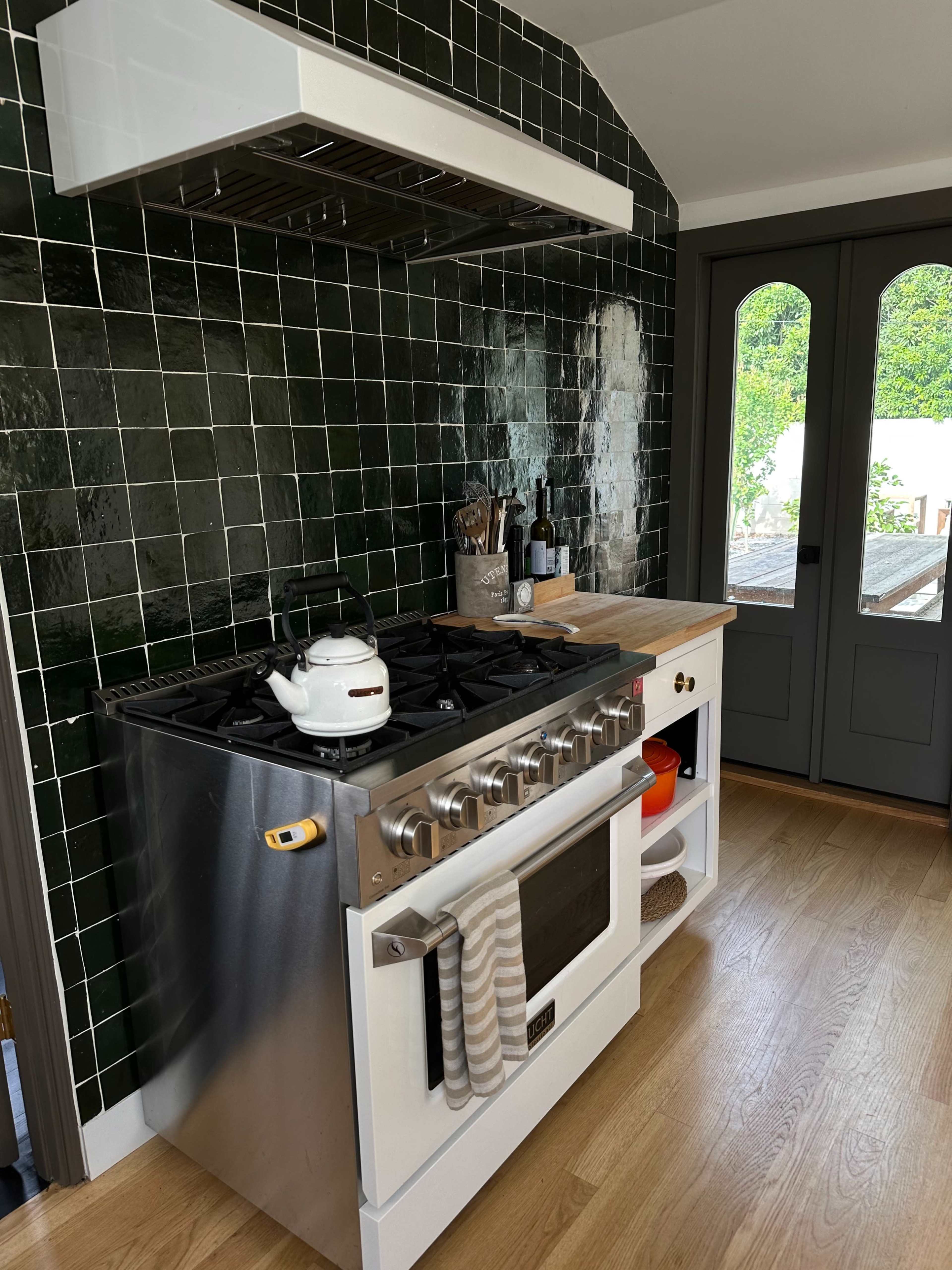 A kitchen with a stainless steel range, a white cabinet beneath it, and a green tiled backsplash.