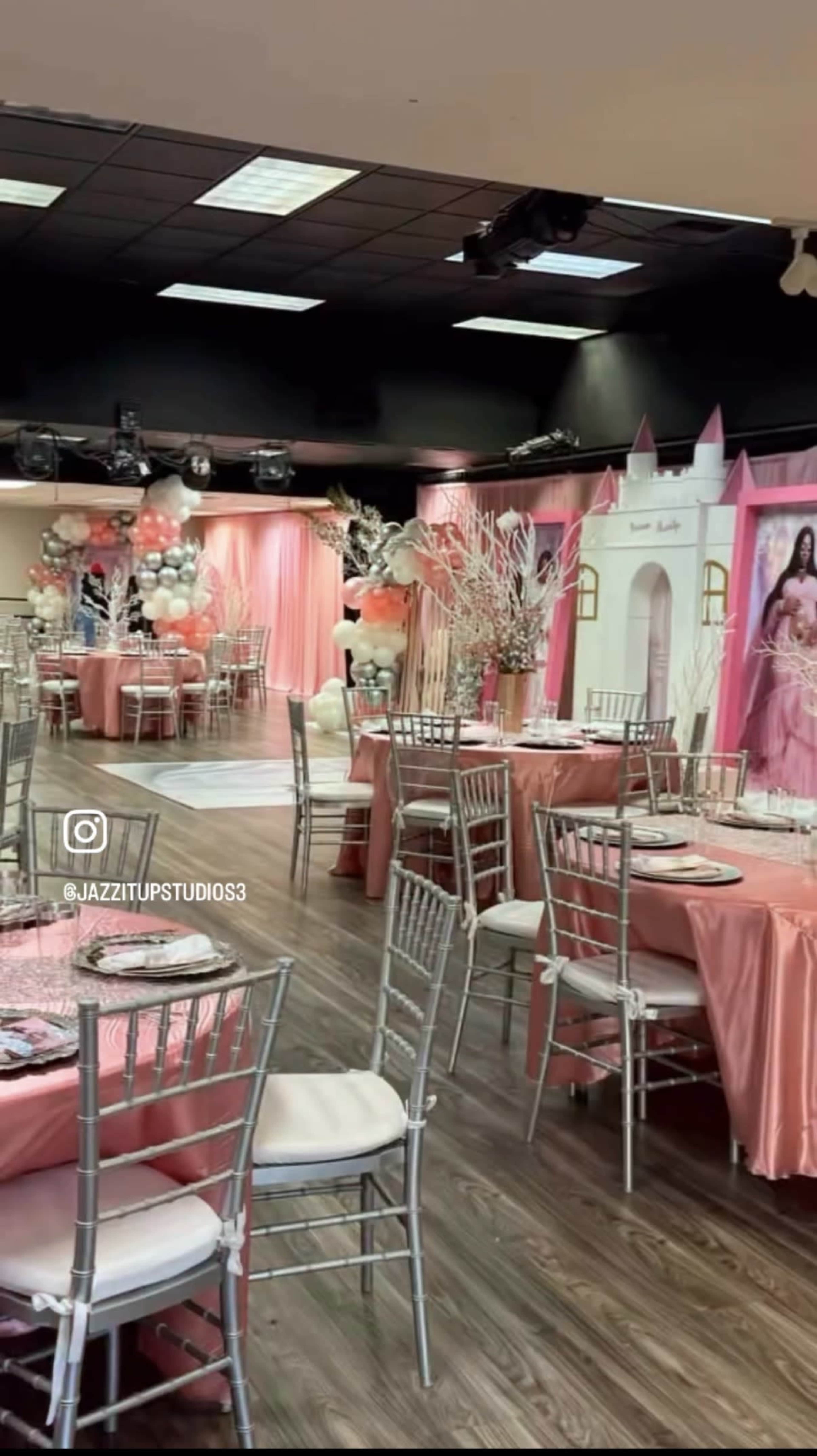 The image shows a decorated event space with pink decorations, tables set with silverware, and a backdrop featuring a princess theme.