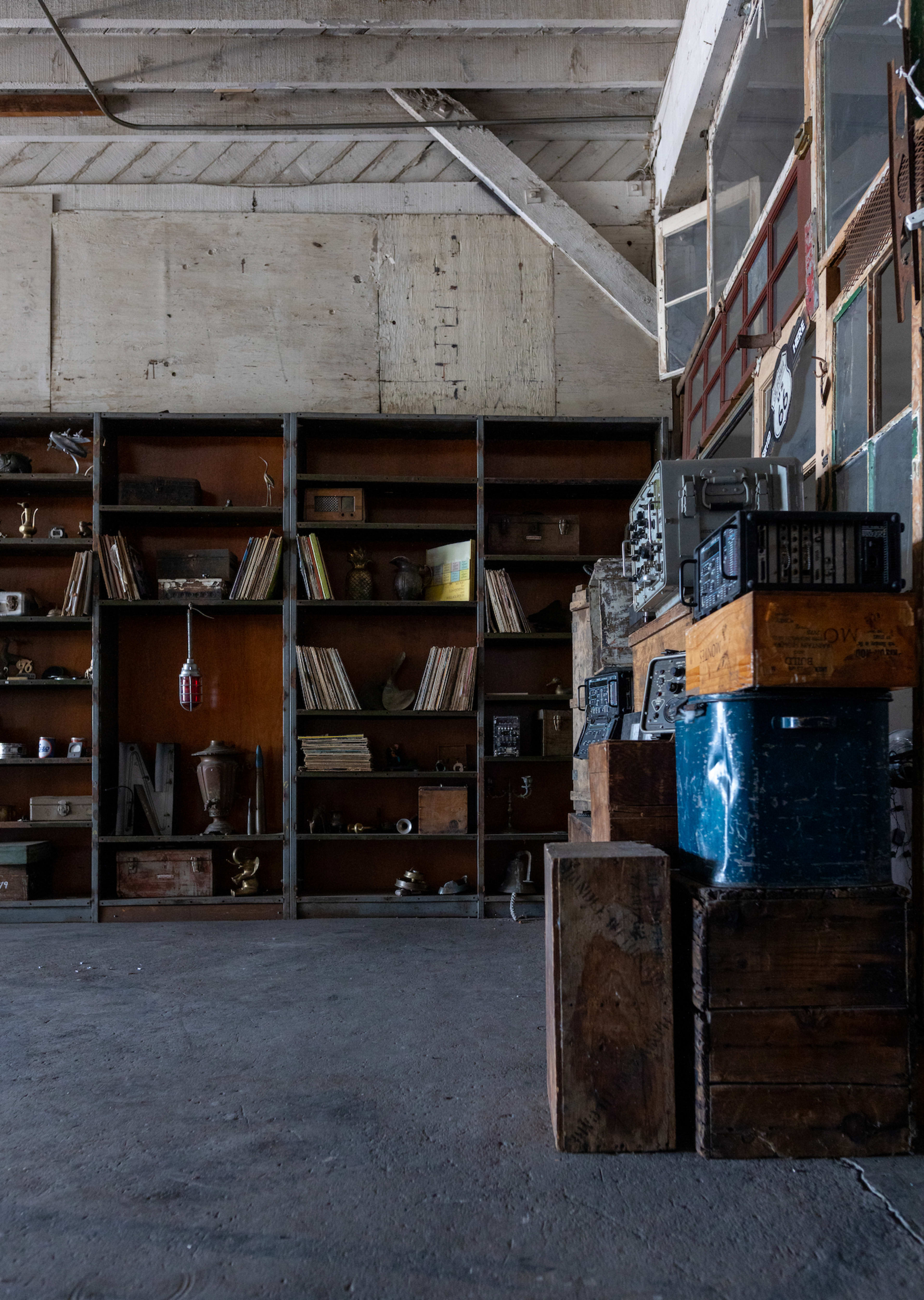 The image shows a dimly lit interior with a wall of shelves filled with books and various artifacts, alongside wooden crates arranged on the floor.