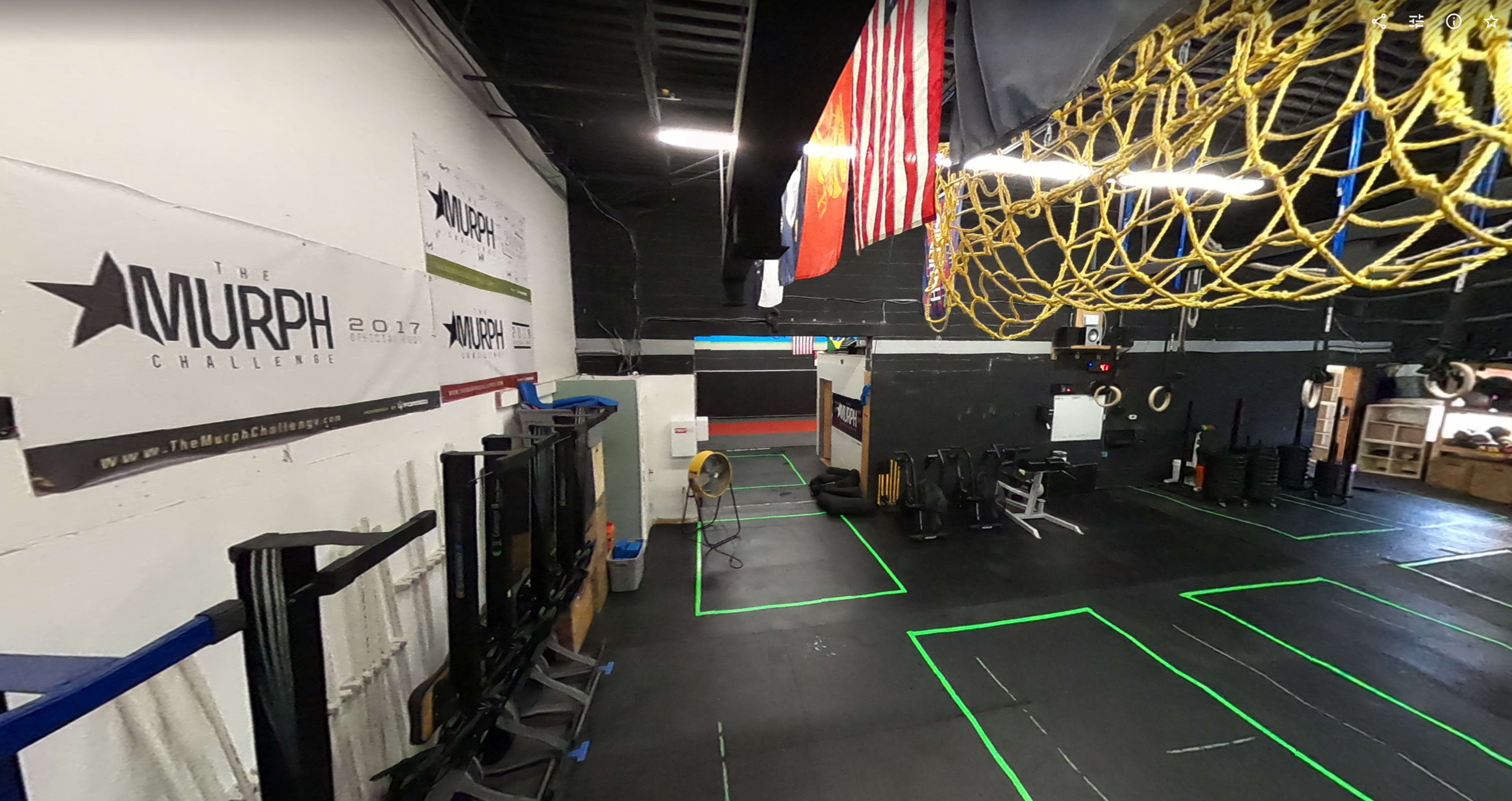 A gym interior with workout equipment, rigging, and banners for "The Murph Challenge" on the walls, along with a flag hanging from the ceiling.
