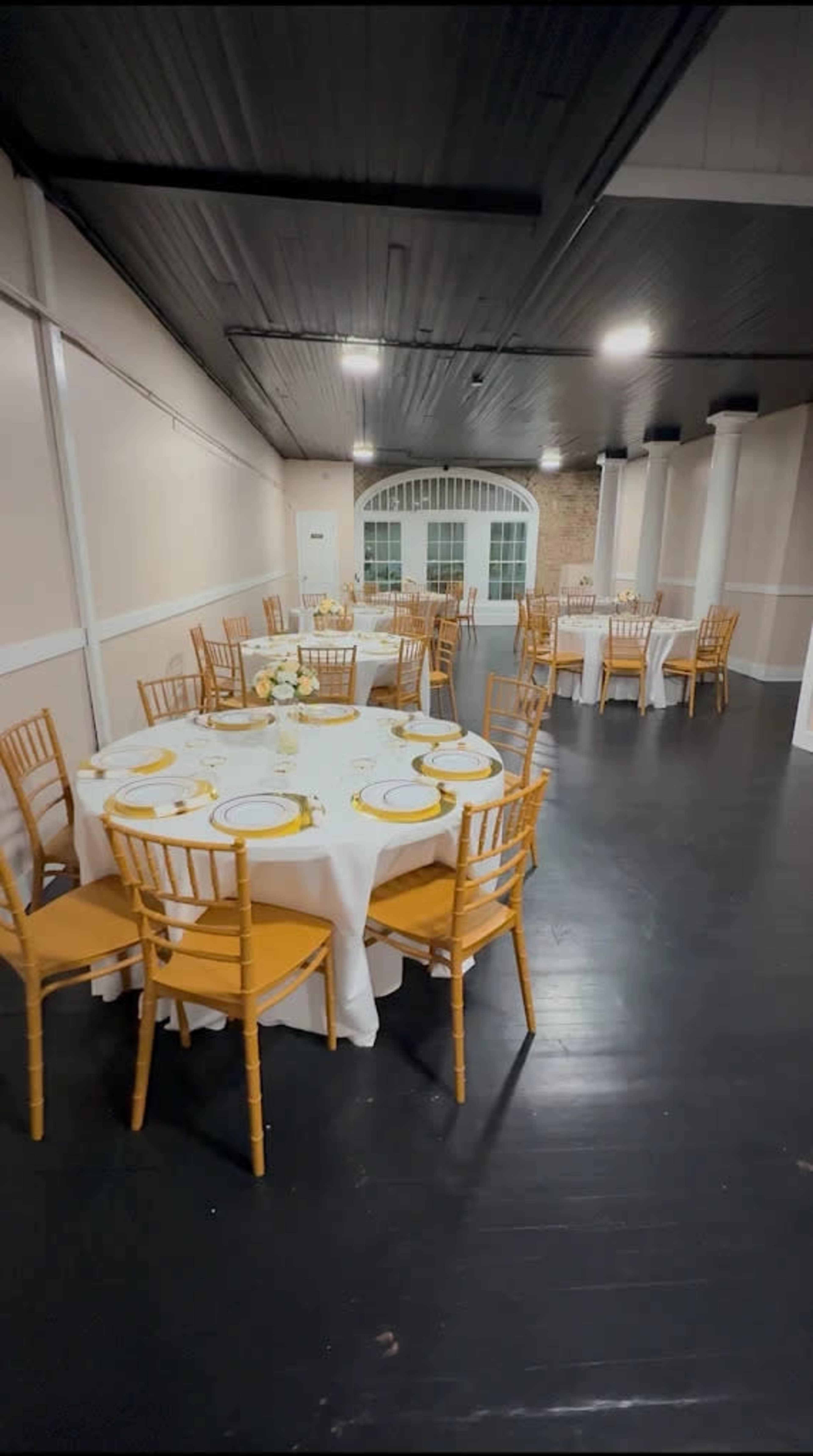 A dining area is arranged with multiple round tables, each set with white tablecloths and yellow accent chairs, in a well-lit space.
