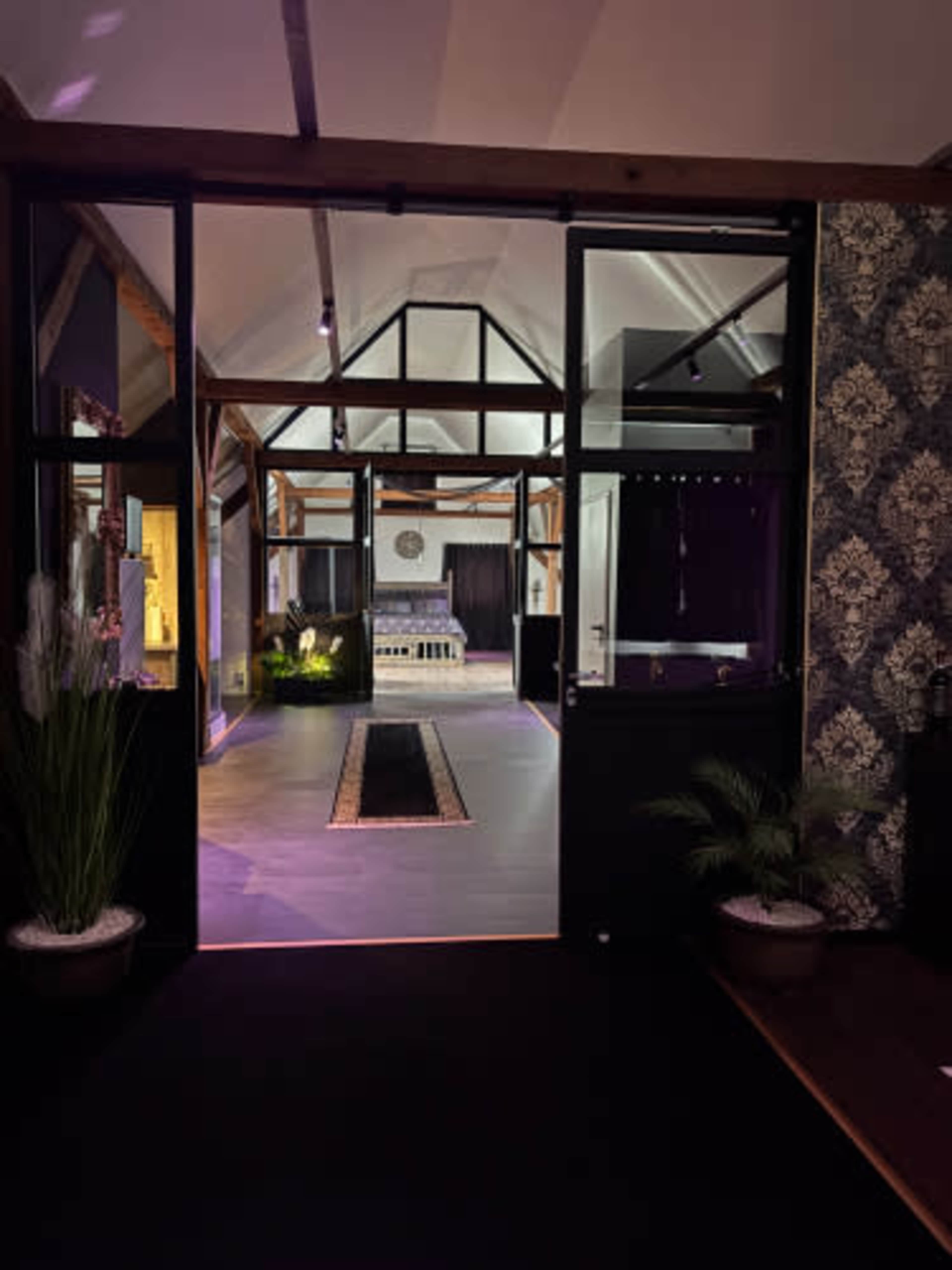 The image shows the entrance of a modern, open-concept space with a view of a well-lit room featuring a bed and decorative elements.