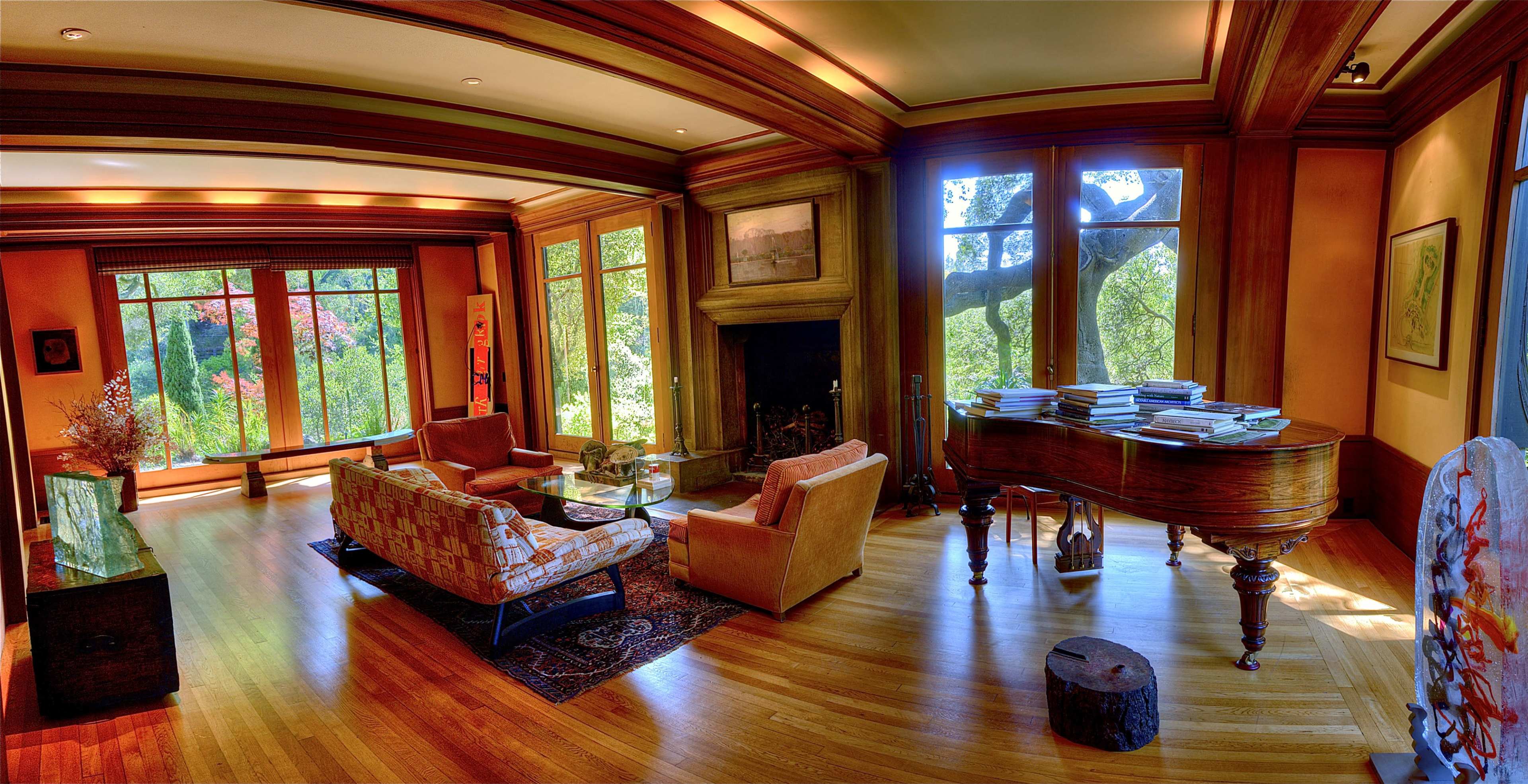 A spacious living room featuring large windows that provide a view of a garden, a grand piano, and seating areas with a wooden floor.