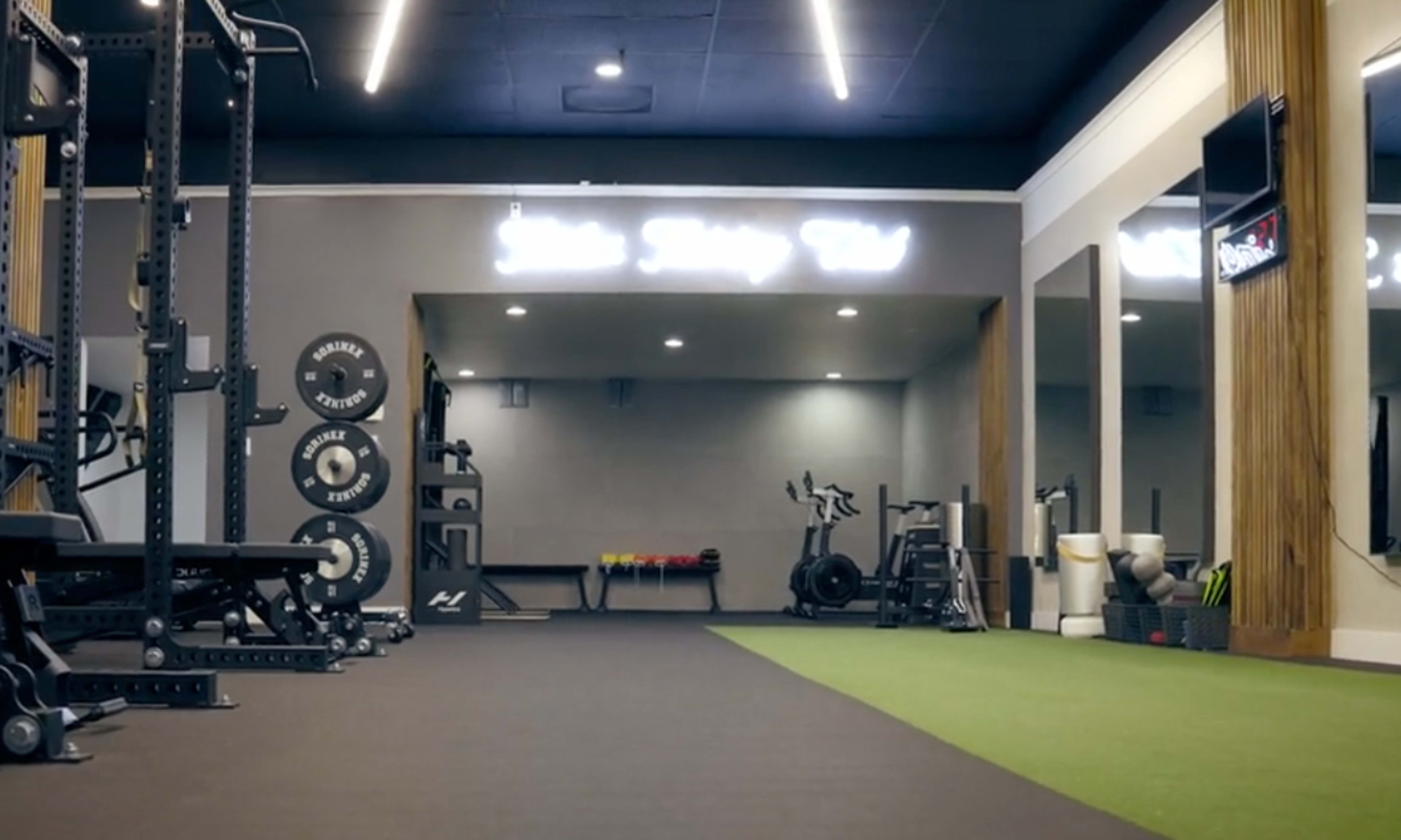 A well-equipped gym featuring strength training machines, free weights, and exercise bikes, with mirrored walls and a turf workout area.