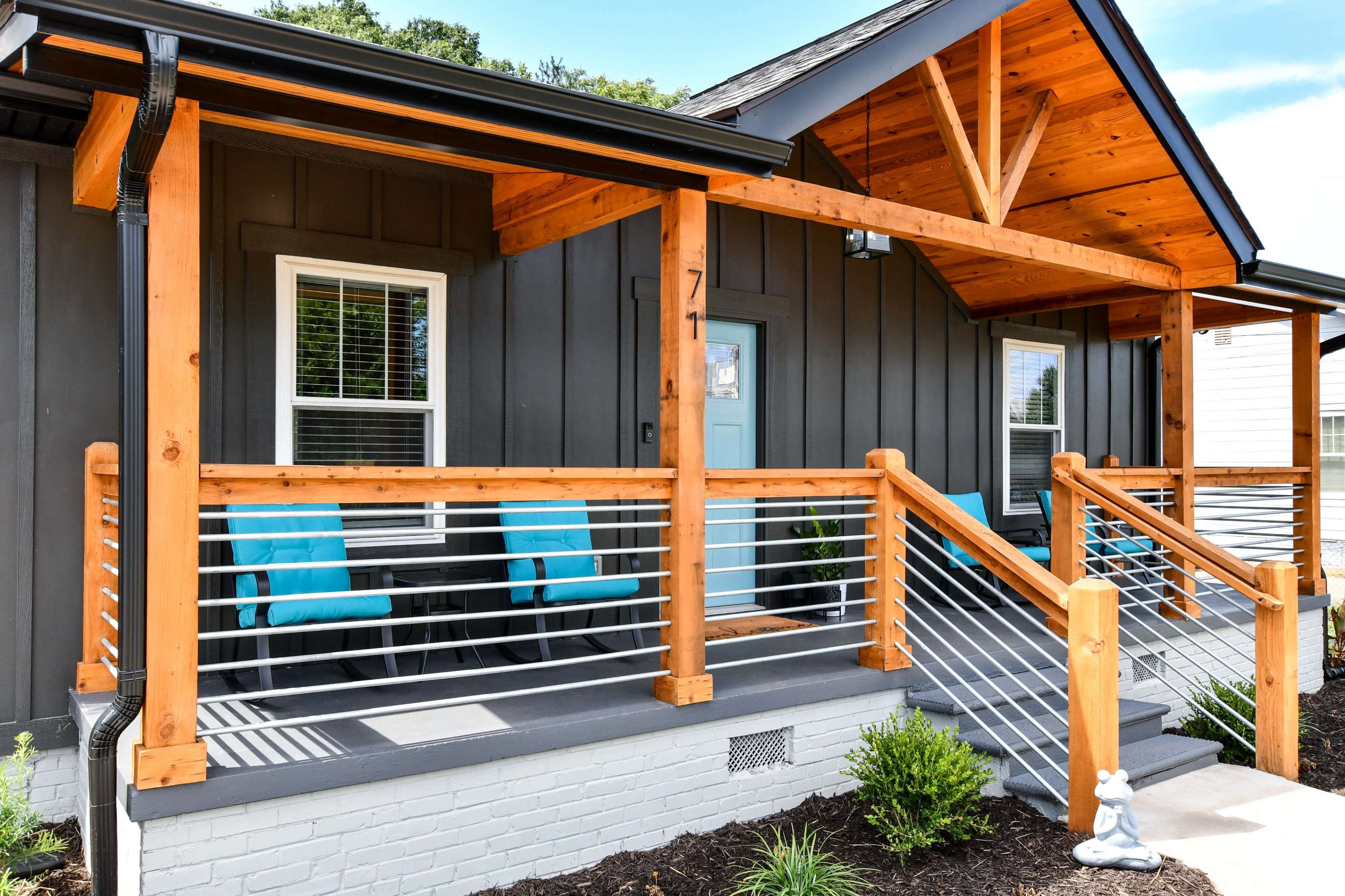 A house with a wooden porch featuring a railing, two blue chairs, and a small decorative statue near the entrance.