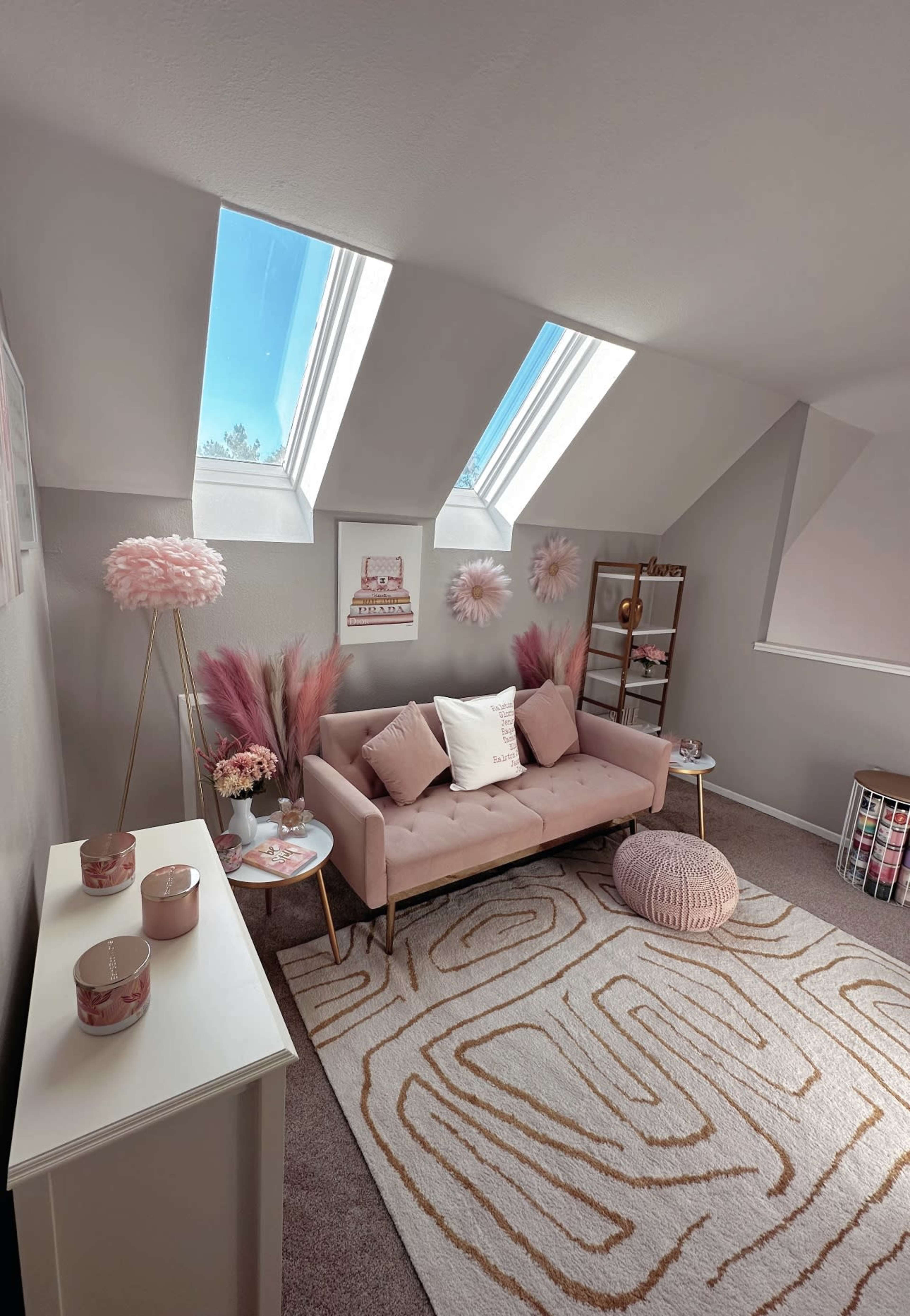 A cozy room features a pink sofa, decorative pillows, and a white rug with an abstract pattern, complemented by skylights and wall decorations.
