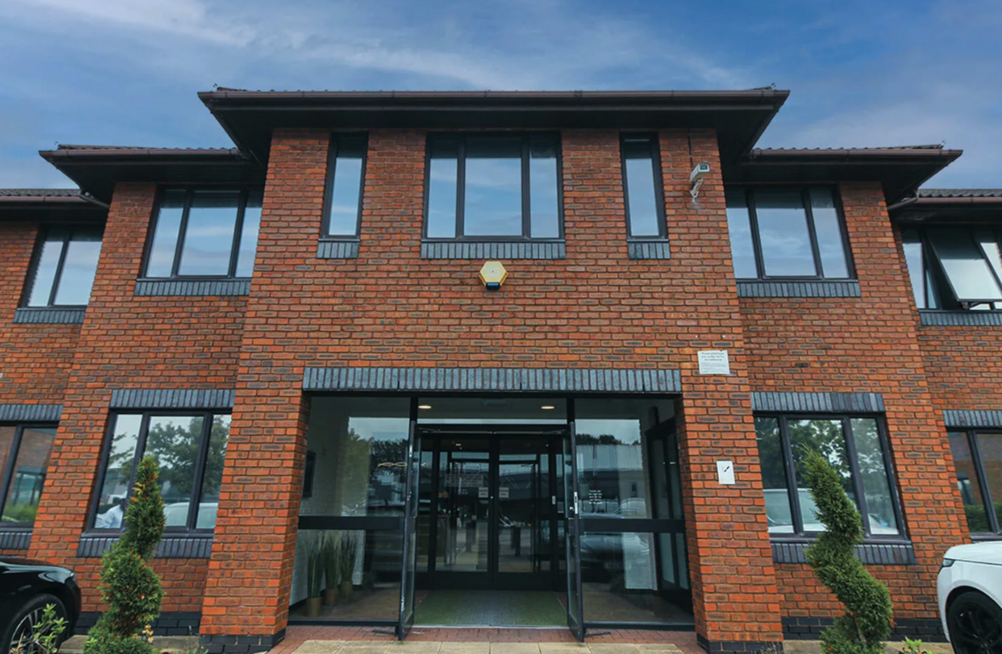 The image shows a modern brick building with a glass entrance and symmetrical windows on either side.
