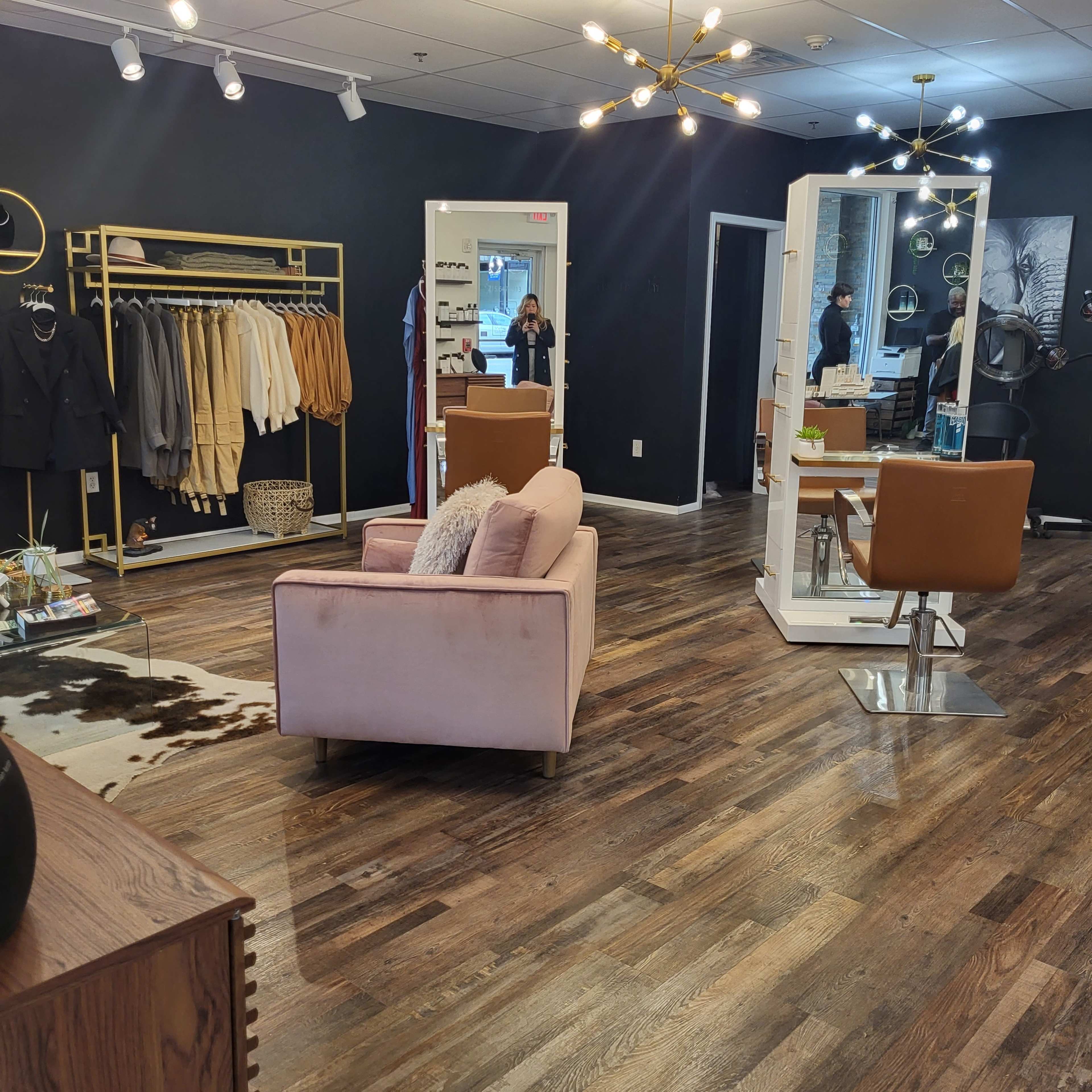 A modern boutique interior with clothing racks, a grooming station, and a seating area featuring a pink sofa.