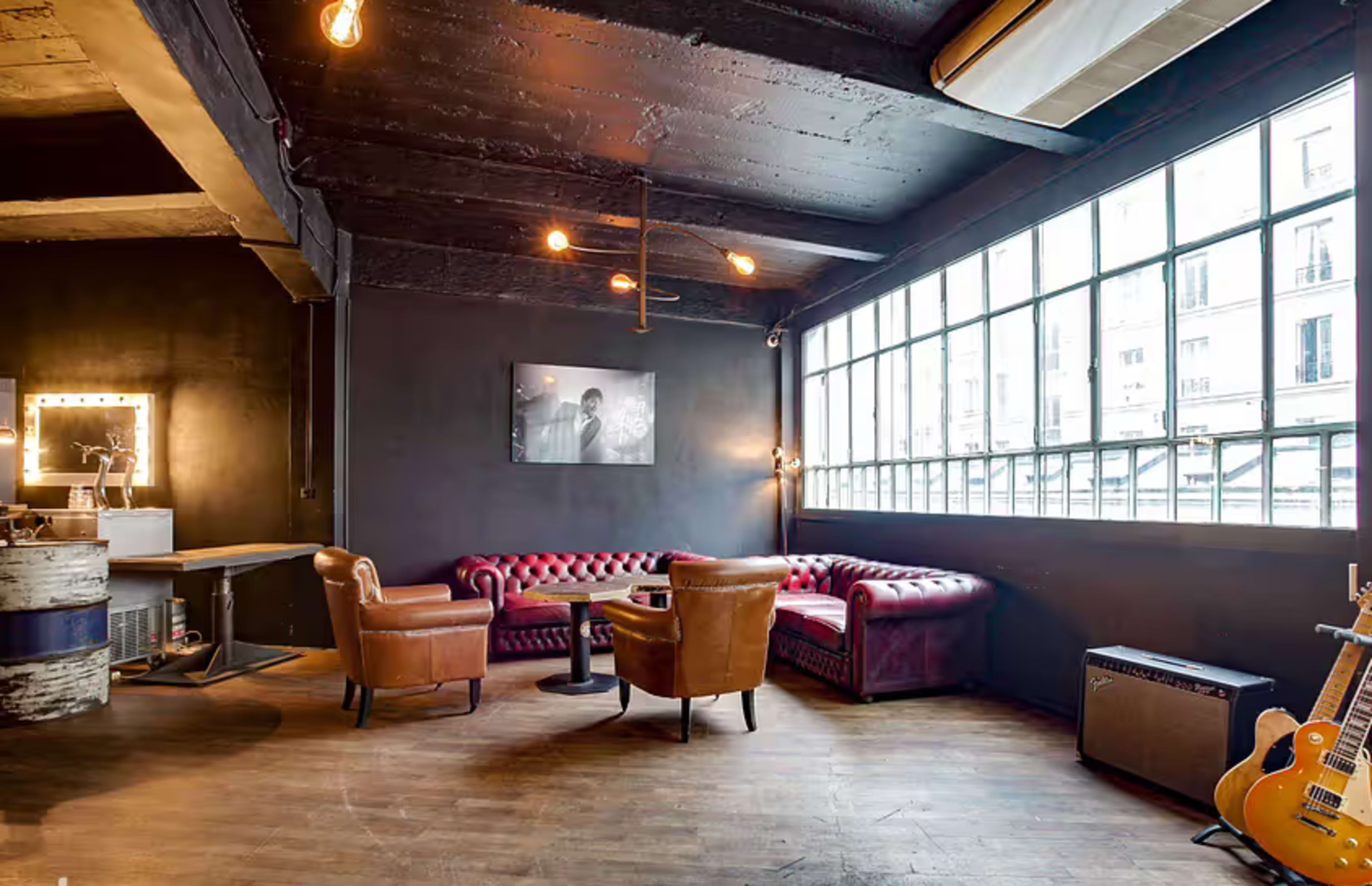 The image shows a stylish lounge area with a leather sofa, two armchairs, a coffee table, and large windows letting in natural light.