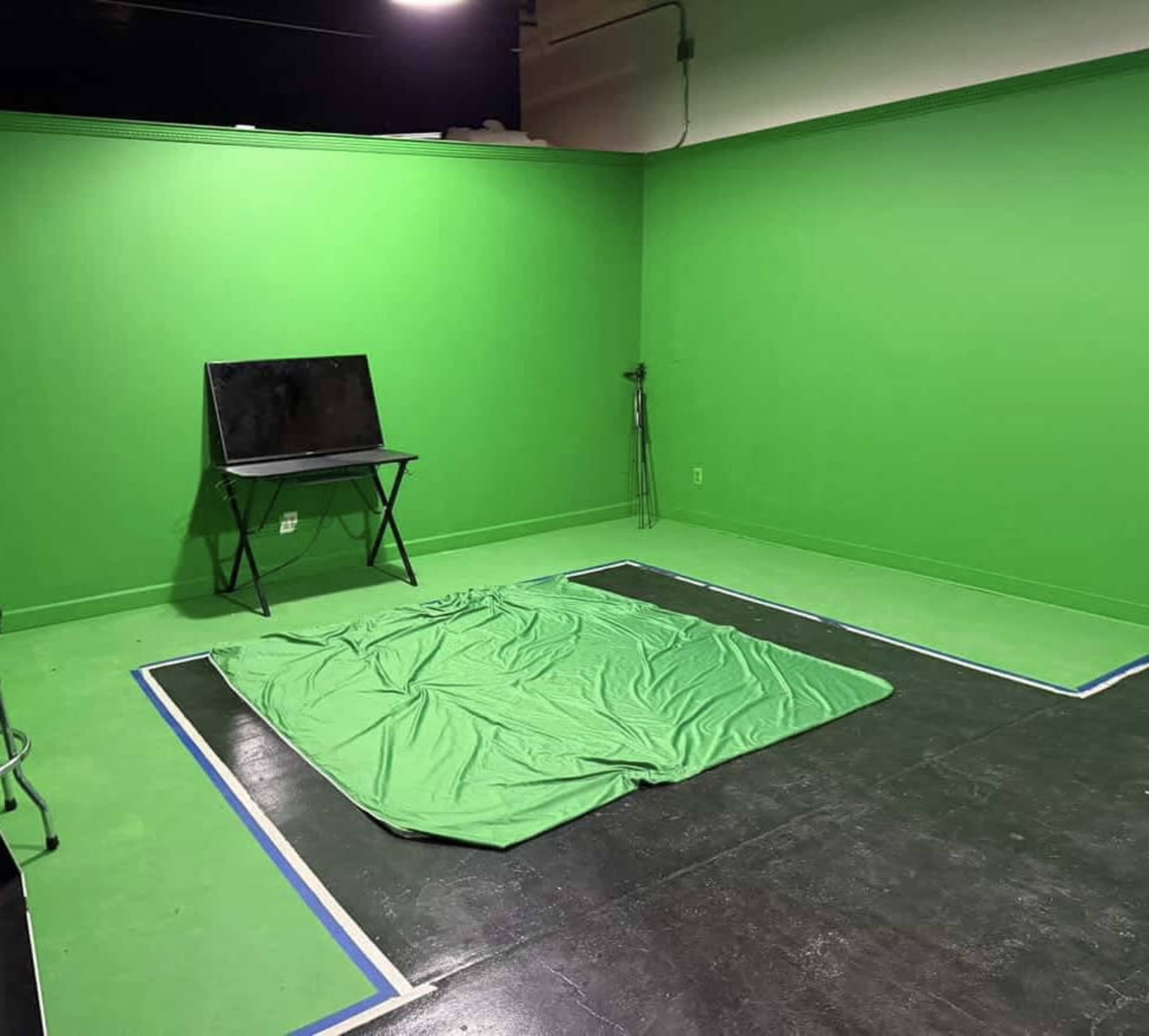 The image shows a green screen studio featuring green walls, a green floor area, and a small black table.
