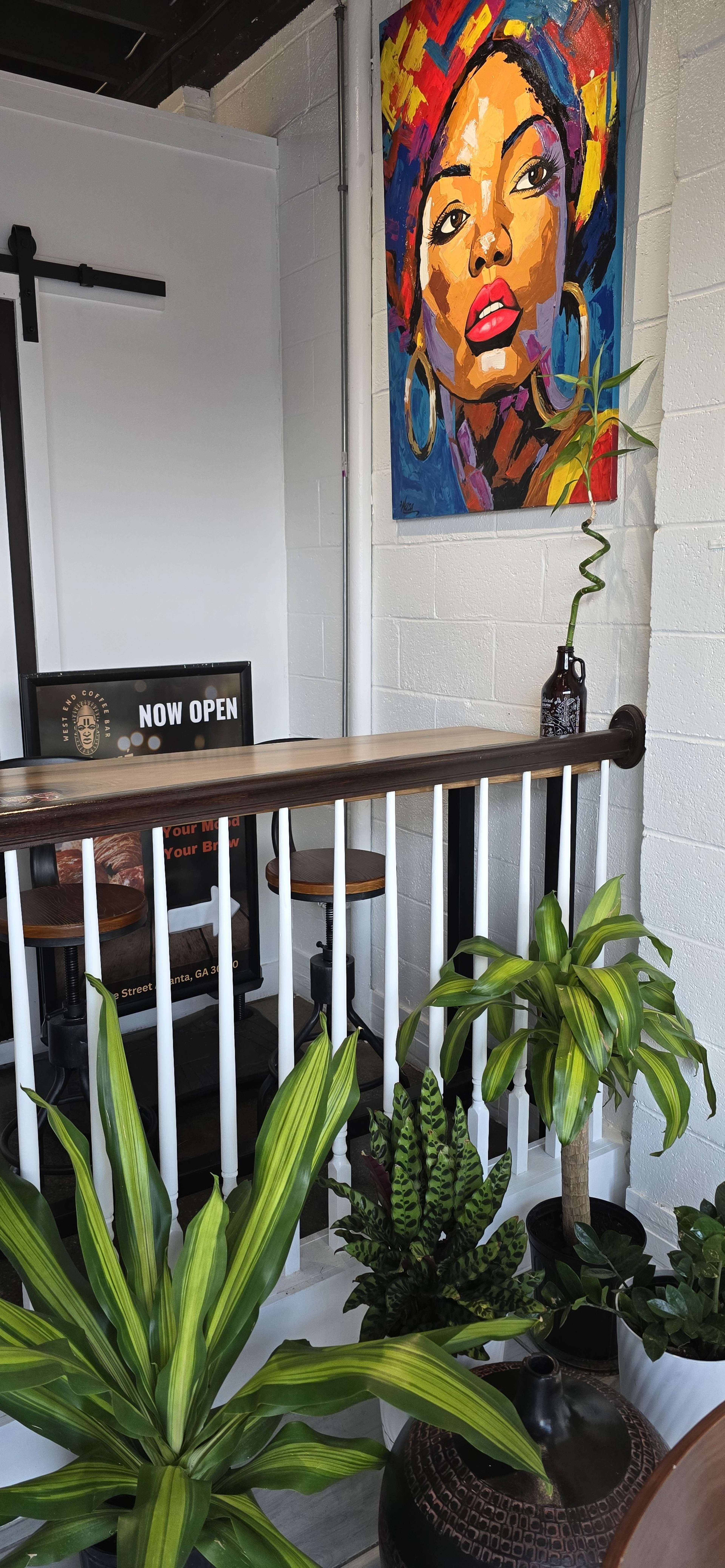 The image shows a vibrant interior space featuring a colorful portrait on the wall, indoor plants, and a "NOW OPEN" sign.