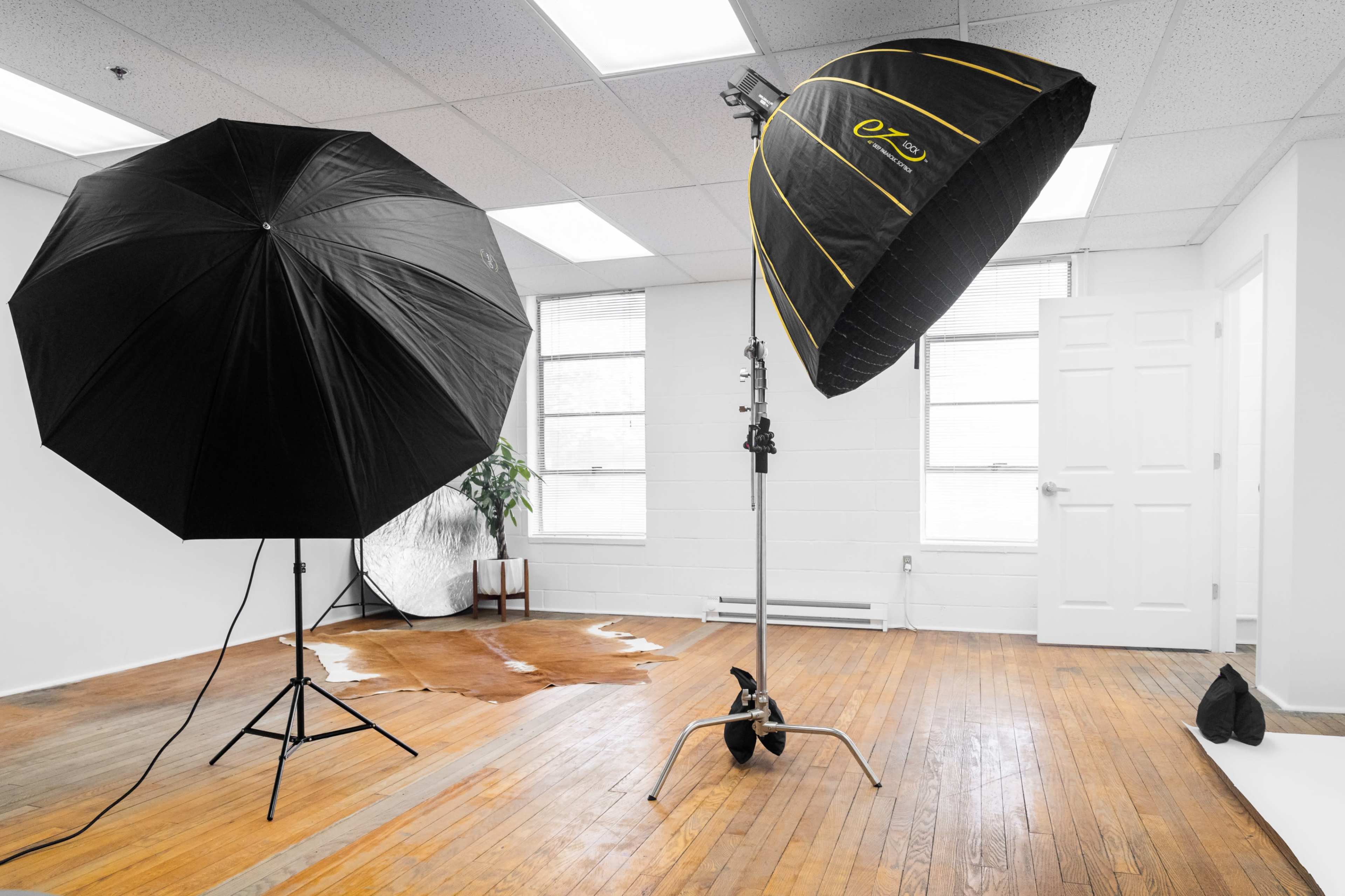 A photography studio with two large black umbrellas, a reflective surface, and a wet patch on the wooden floor.