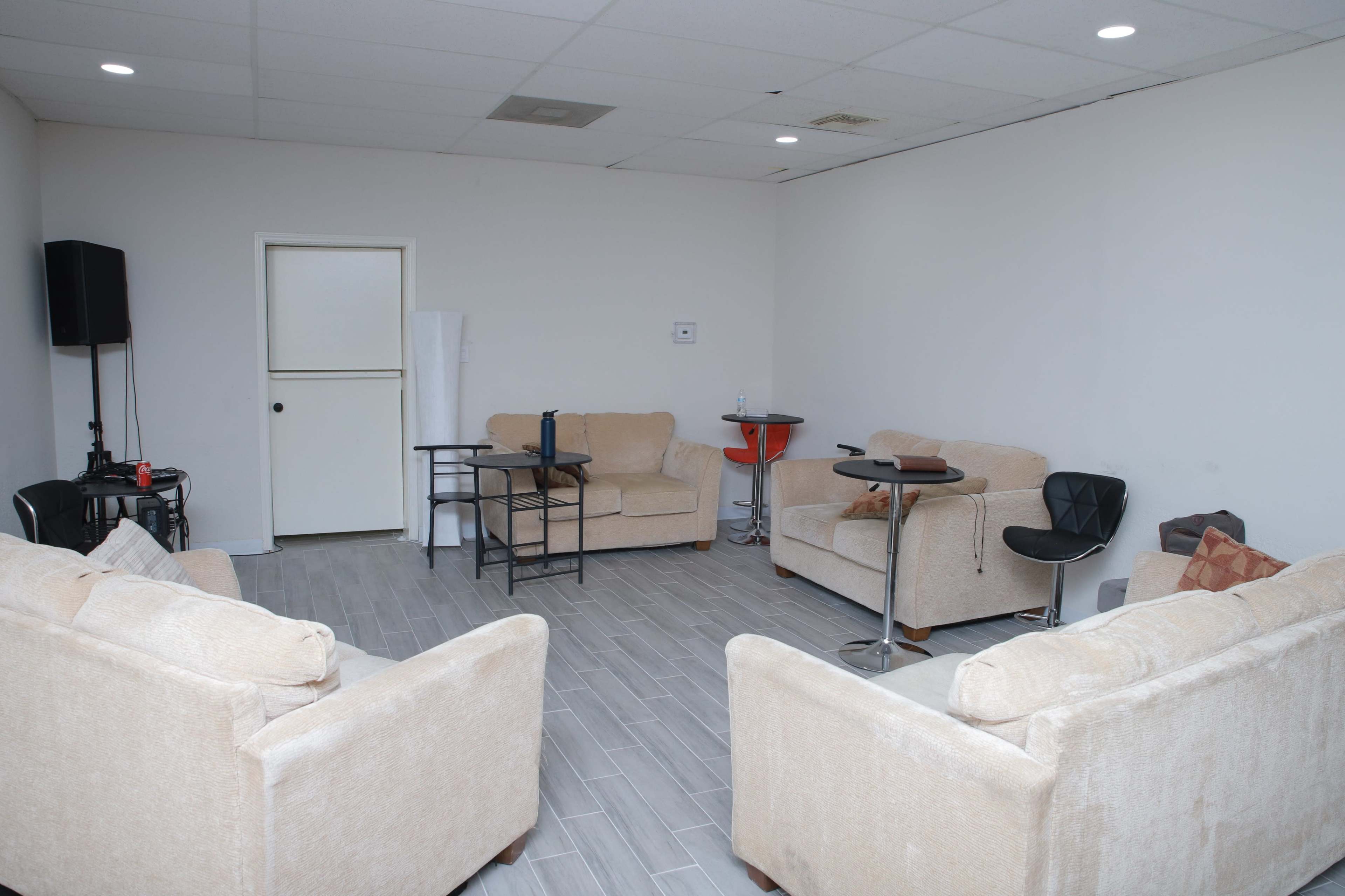 A spacious, uncluttered room features several beige couches arranged around small tables and a door leading to a separate area.