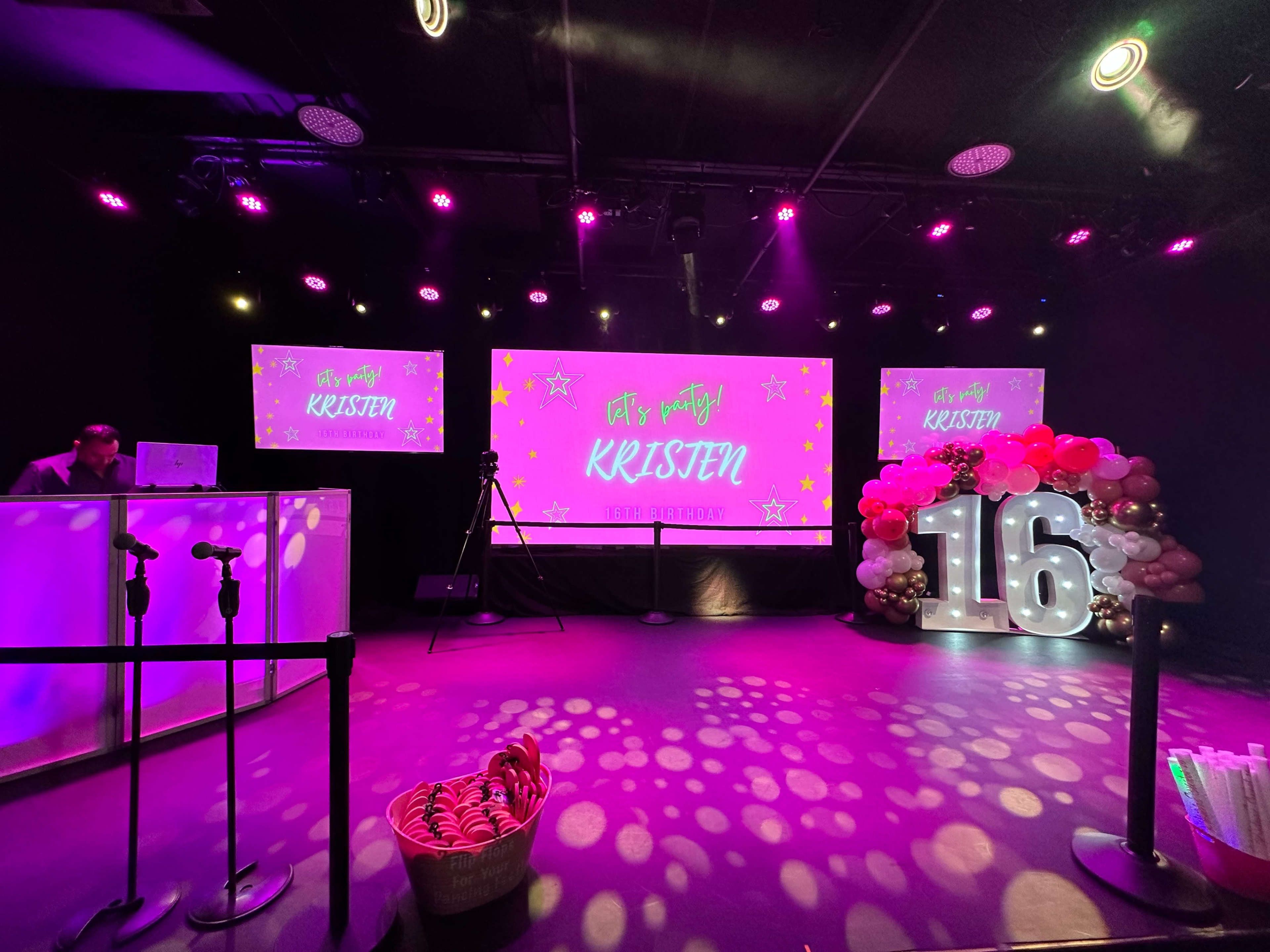 The scene depicts a festive event setup with colorful decorations, a large screen displaying "Let's Party Kristen," and a decorative display with the number 16.