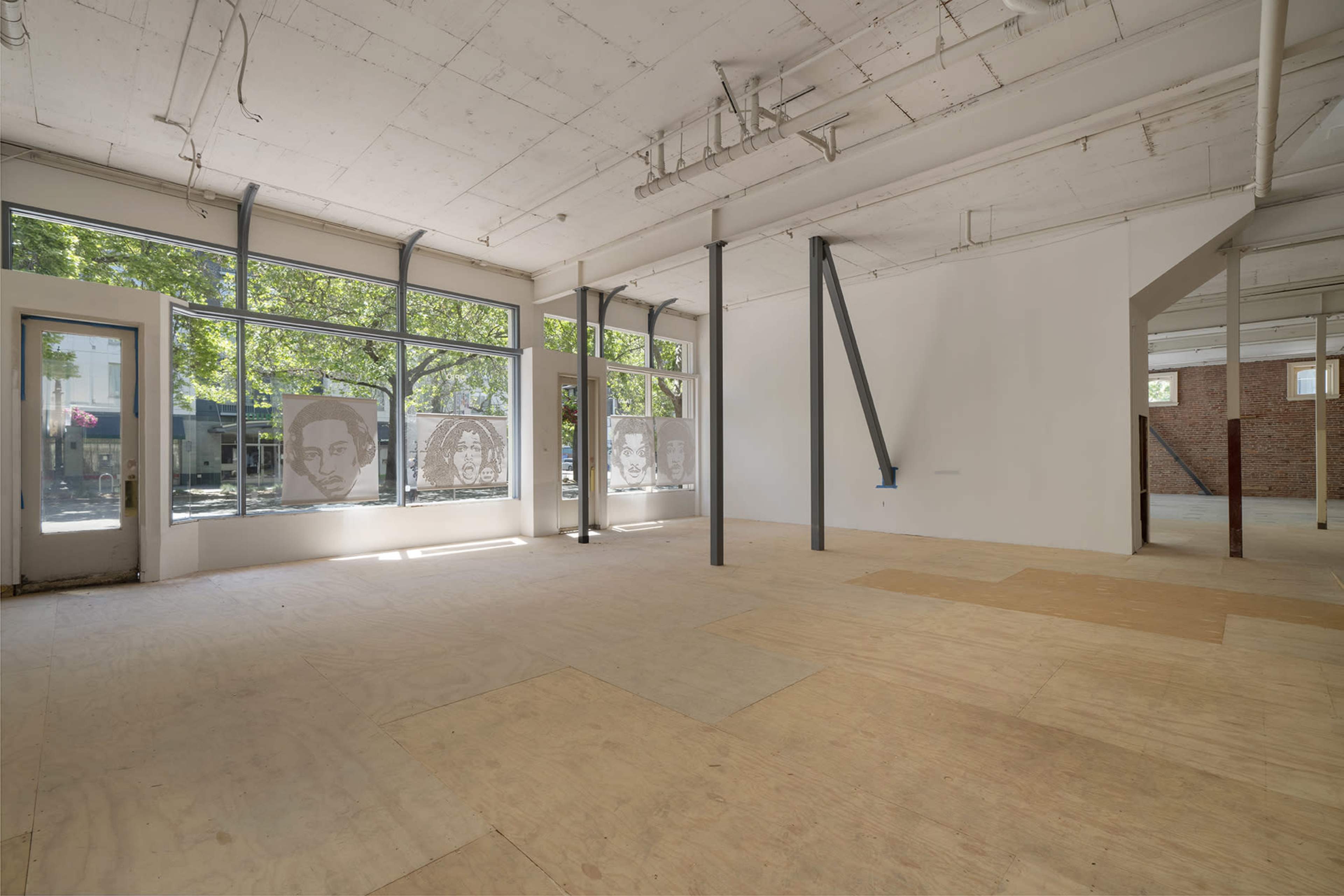 An empty interior space with large windows displaying artwork and exposed structural elements.