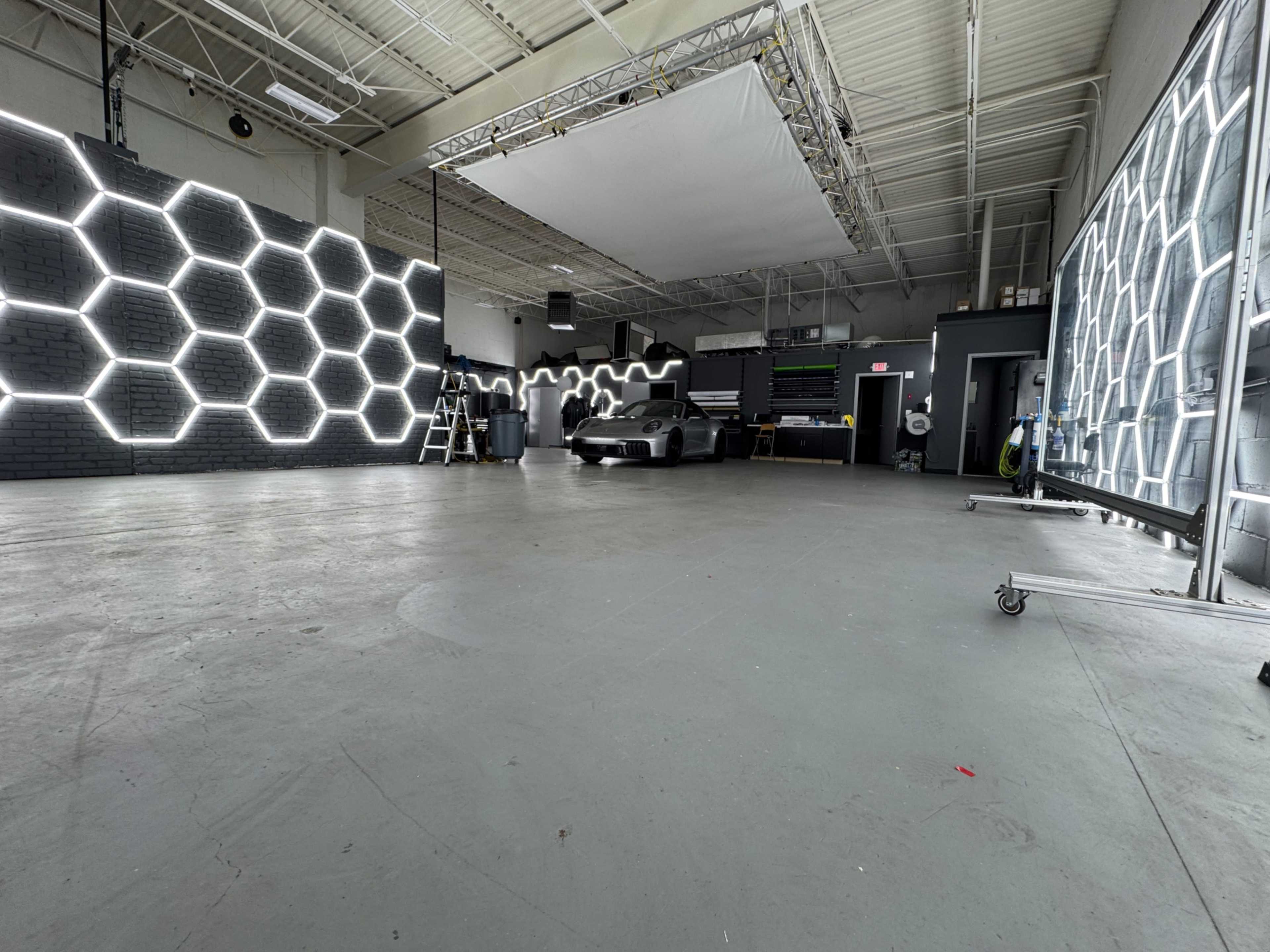 A spacious studio features hexagonal light fixtures on the walls, with a car positioned in the center and various equipment in the background.