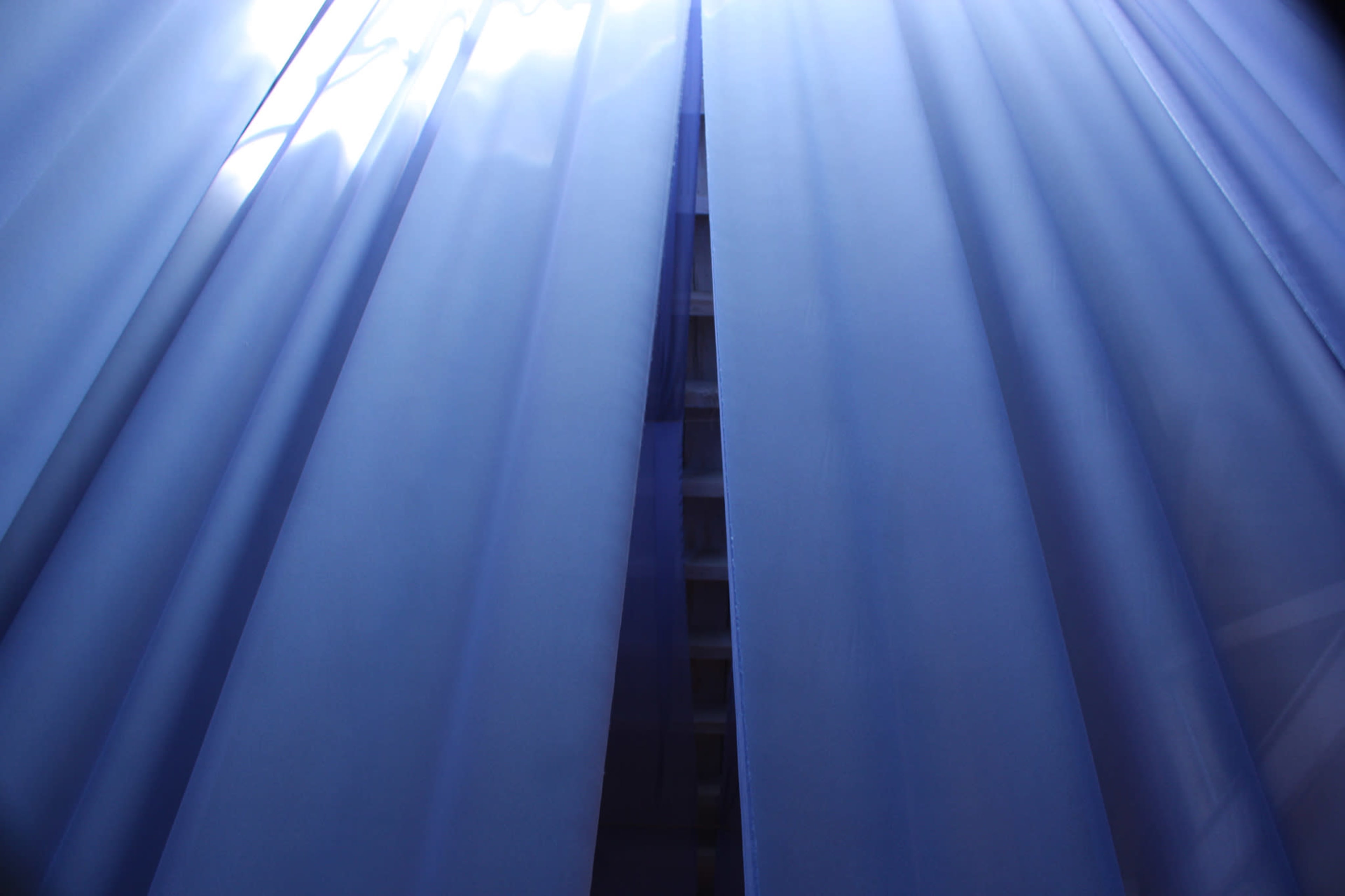 Light filters through sheer blue curtains, revealing a glimpse of a structured surface behind.