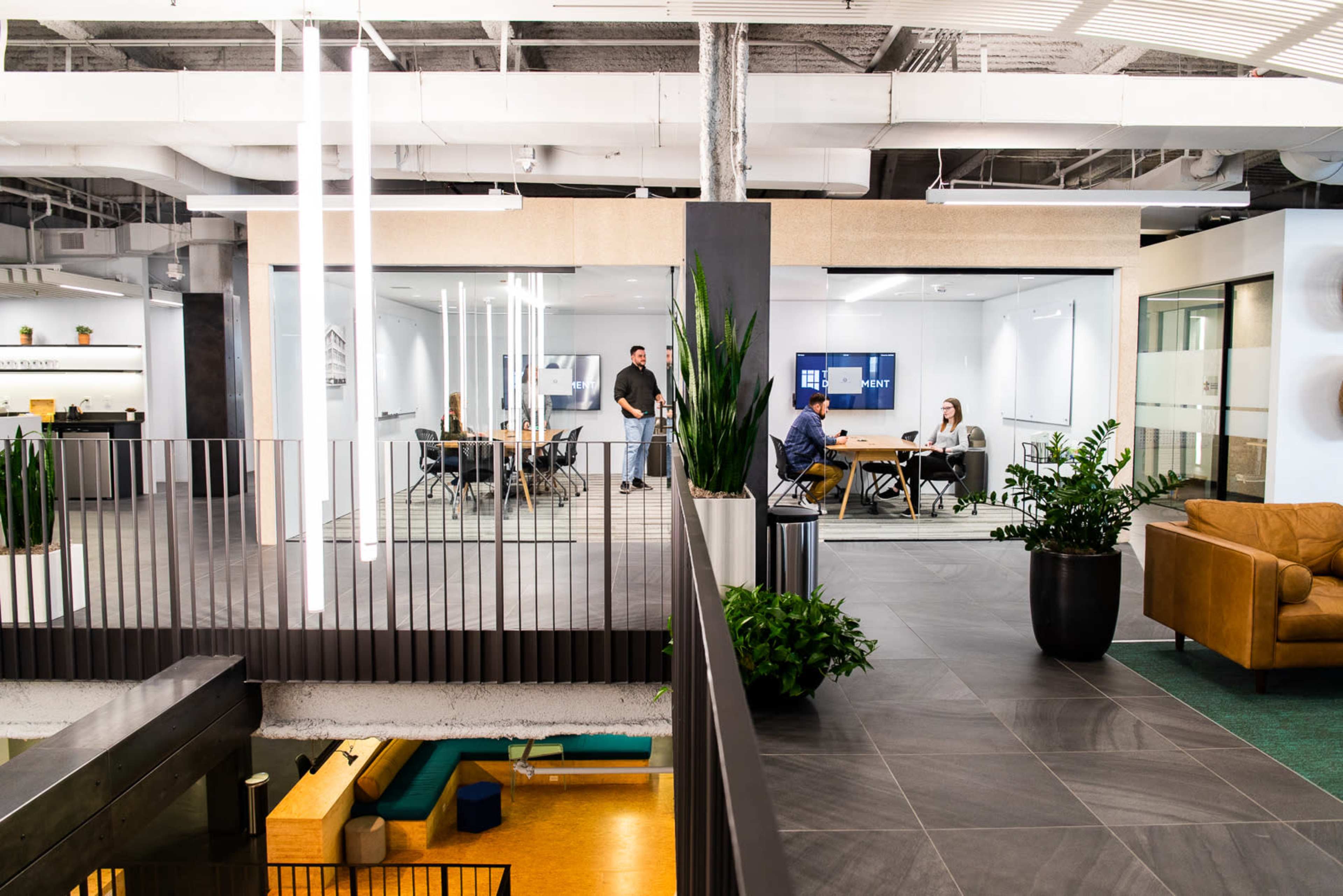 A modern office space with glass meeting rooms, people engaged in discussions, and various seating areas.