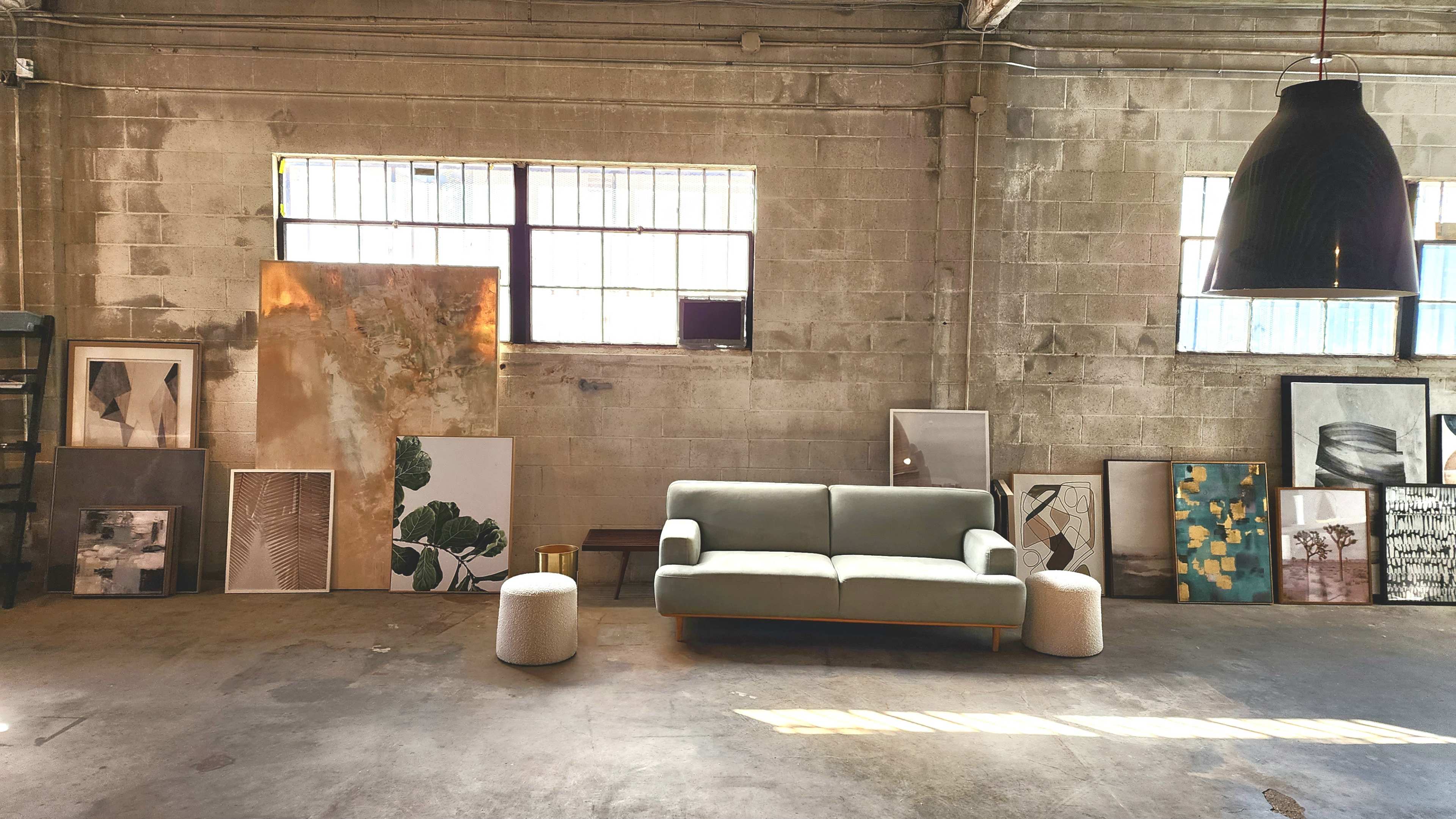A light green sofa sits in the center of an industrial space surrounded by various framed artworks against the walls.