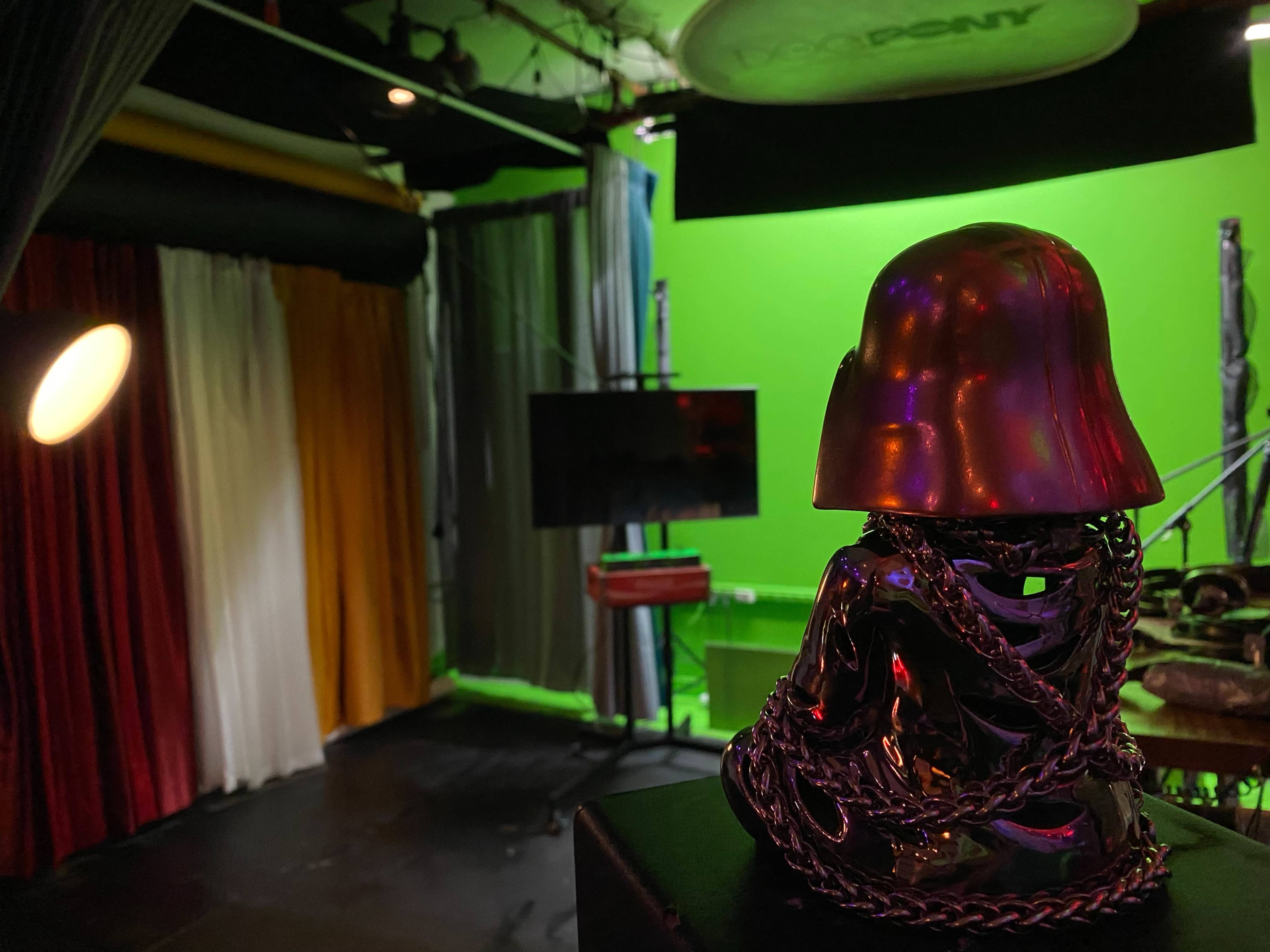 A metallic skull with chains is positioned in the foreground of a studio with colorful curtains and a green backdrop.