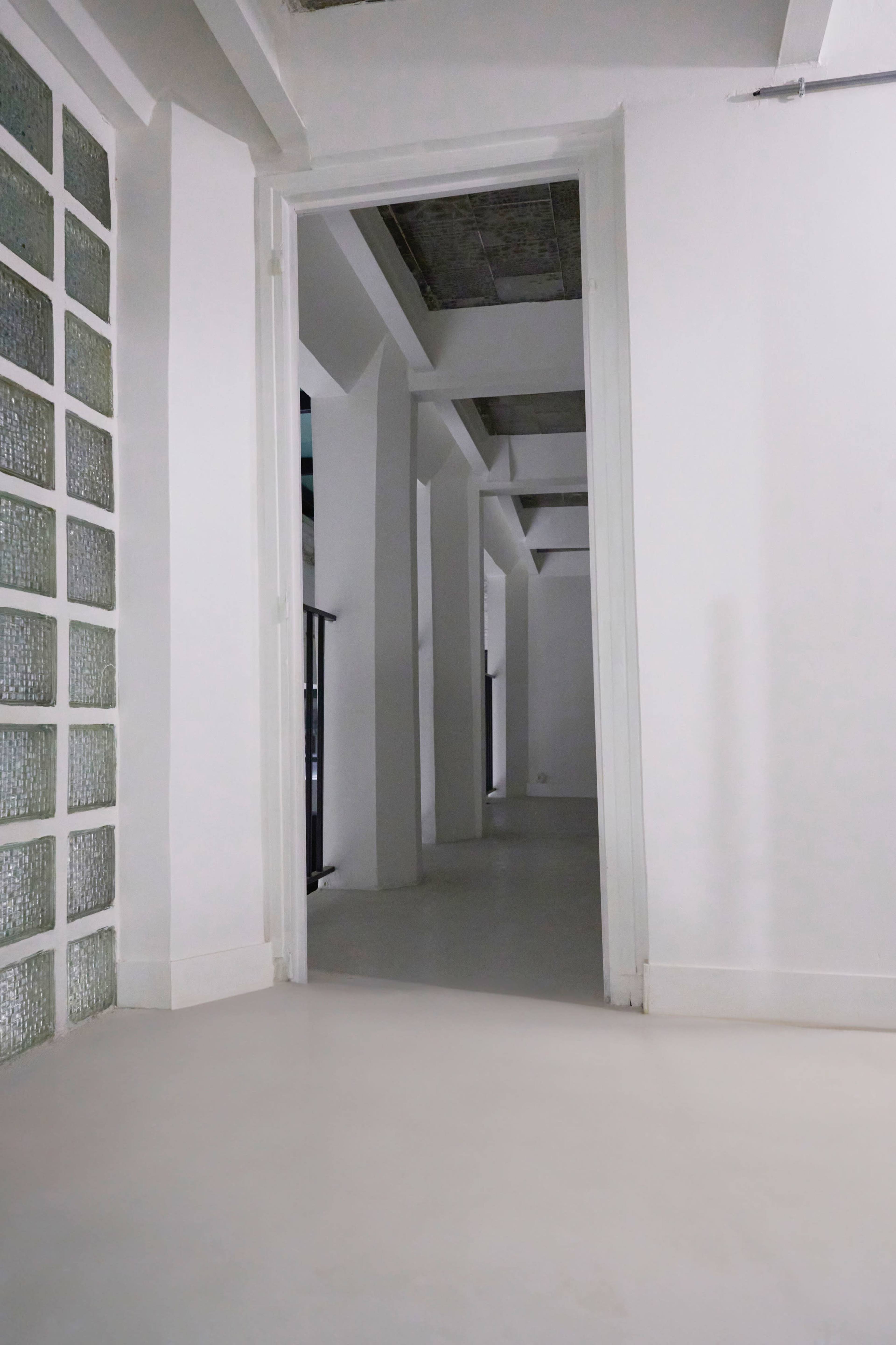 A hallway with white walls, a glass block window, and a view into an adjacent room.