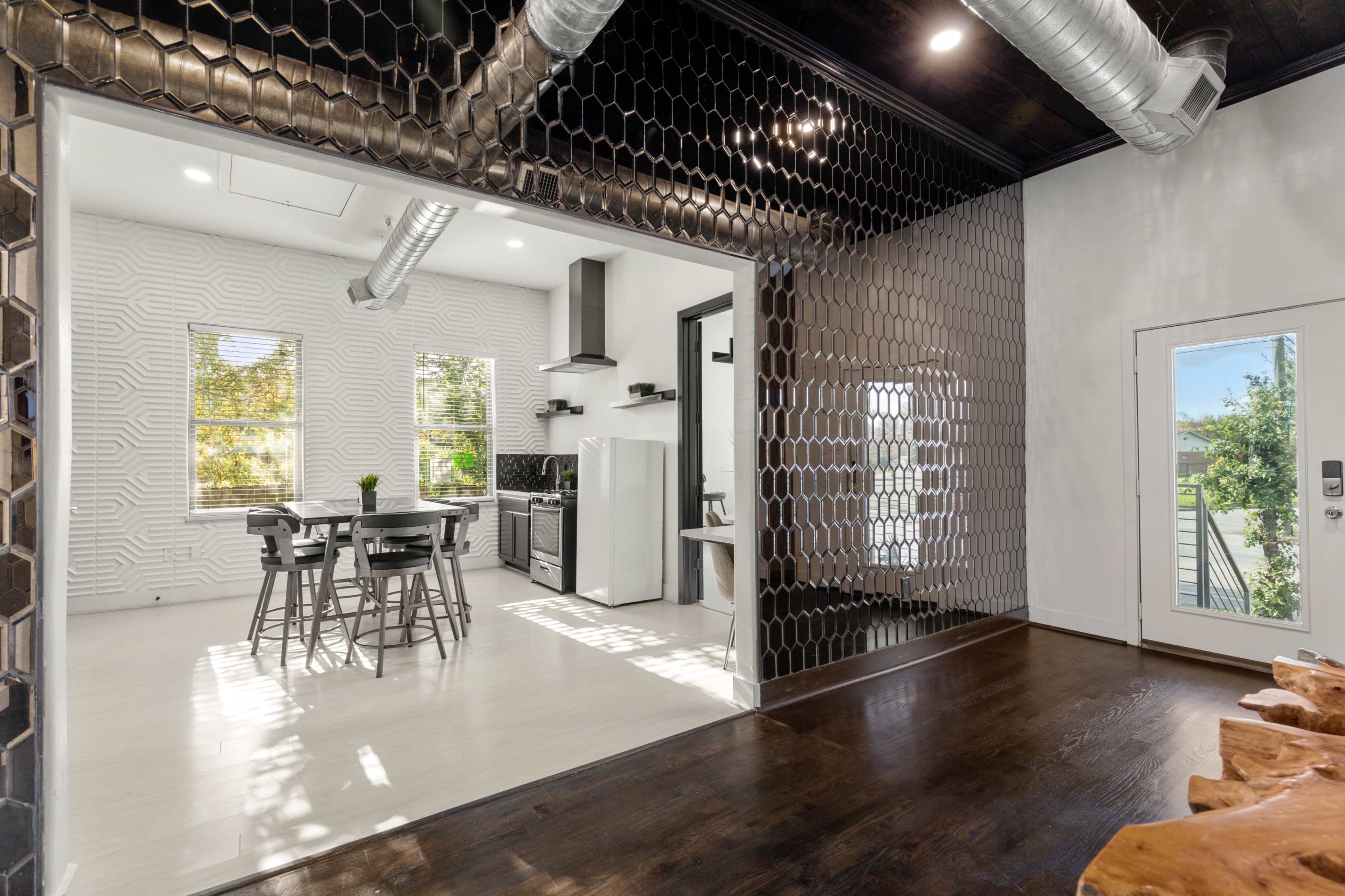 A modern, open-concept kitchen and dining area featuring a honeycomb-patterned wall and large windows allowing natural light to stream in.