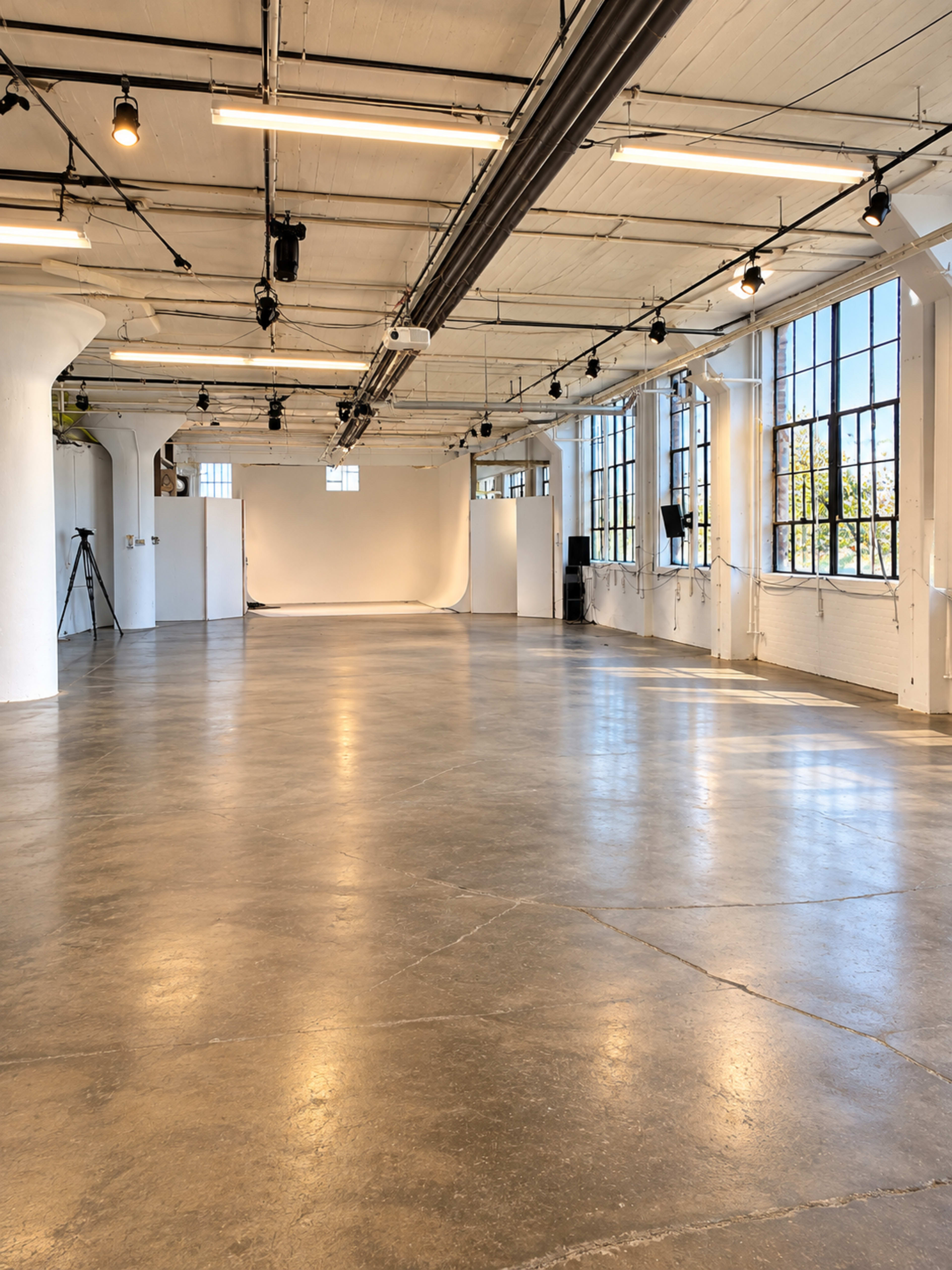 The image shows a spacious, well-lit industrial studio with polished concrete floors and large windows.