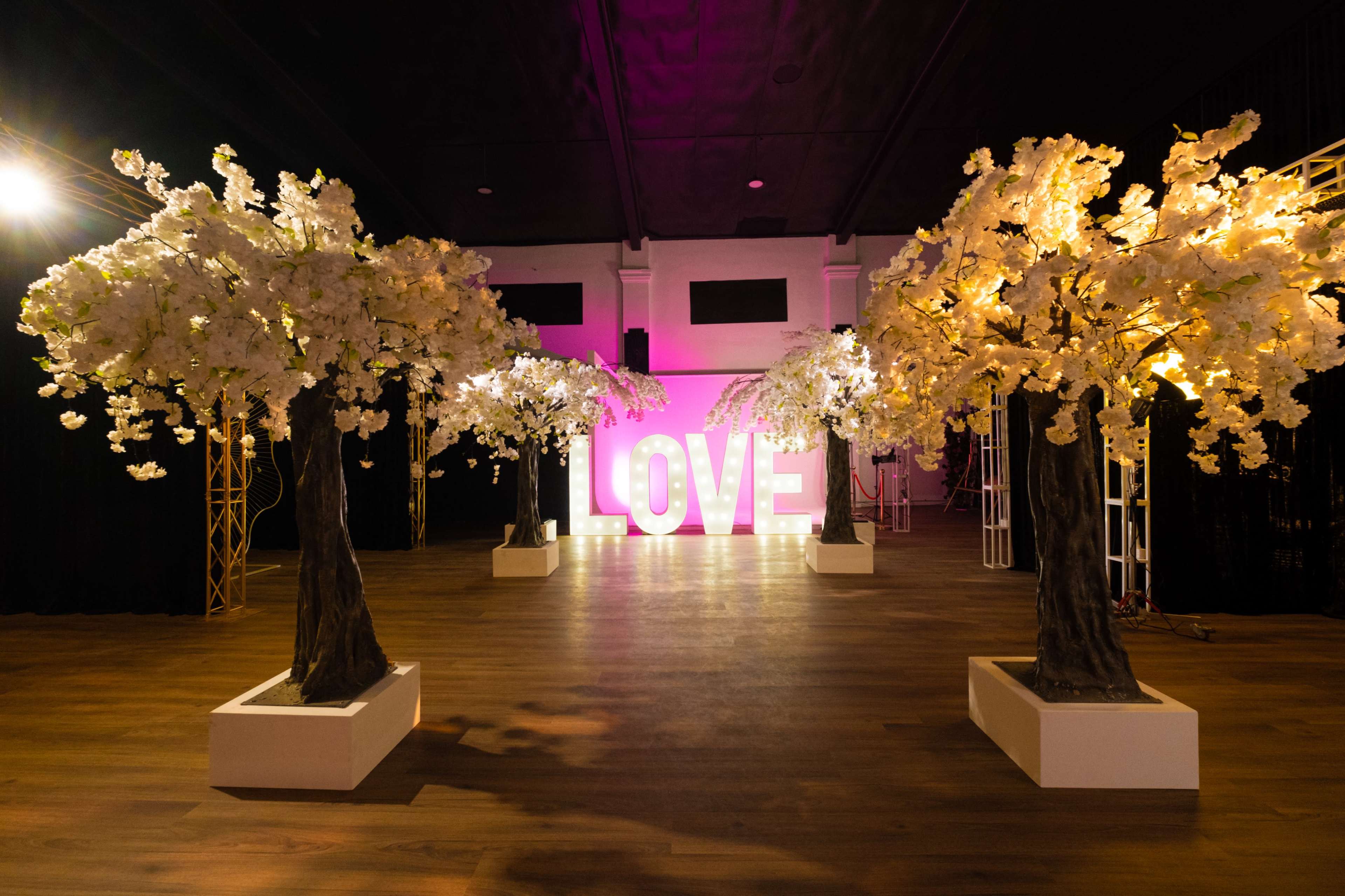 The scene features large illuminated letters spelling "LOVE" flanked by artificial cherry blossom trees in a dimly lit venue.