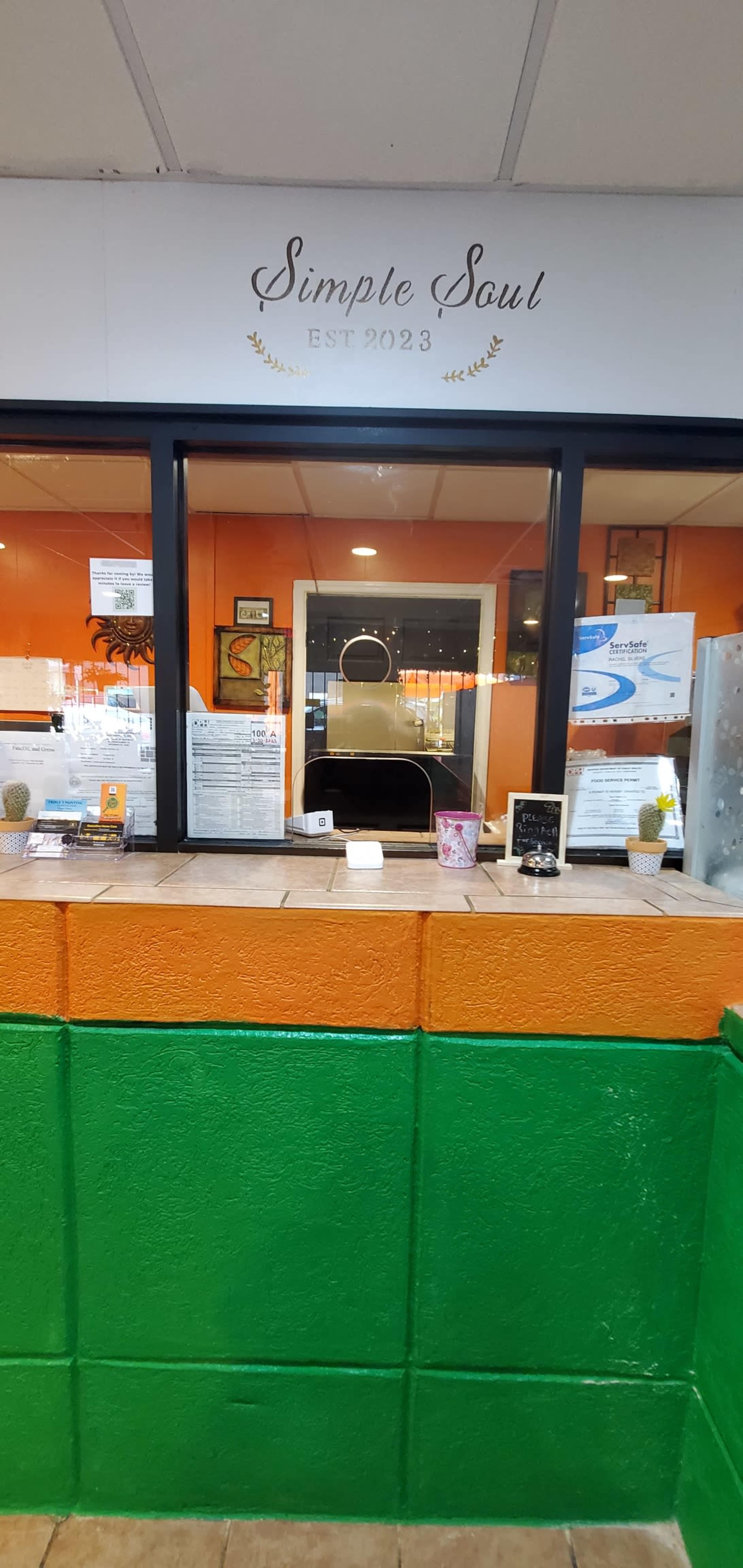 A service counter marked "Simple Soul" with an orange and green color scheme and various documents displayed in front of a window.