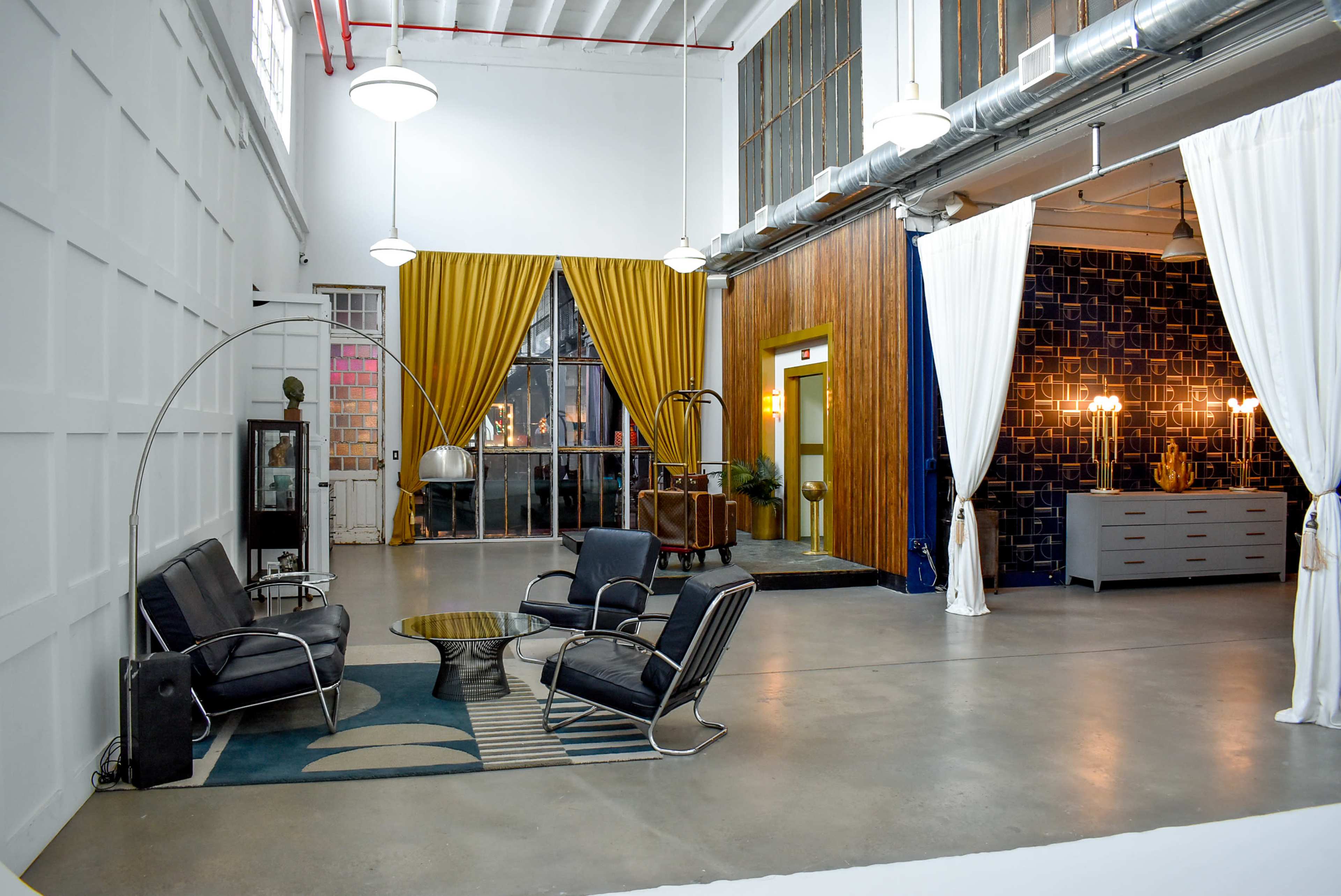 A spacious interior with modern furniture, featuring a seating area with black chairs and a round table, separated by decorative curtains and walls in various colors.