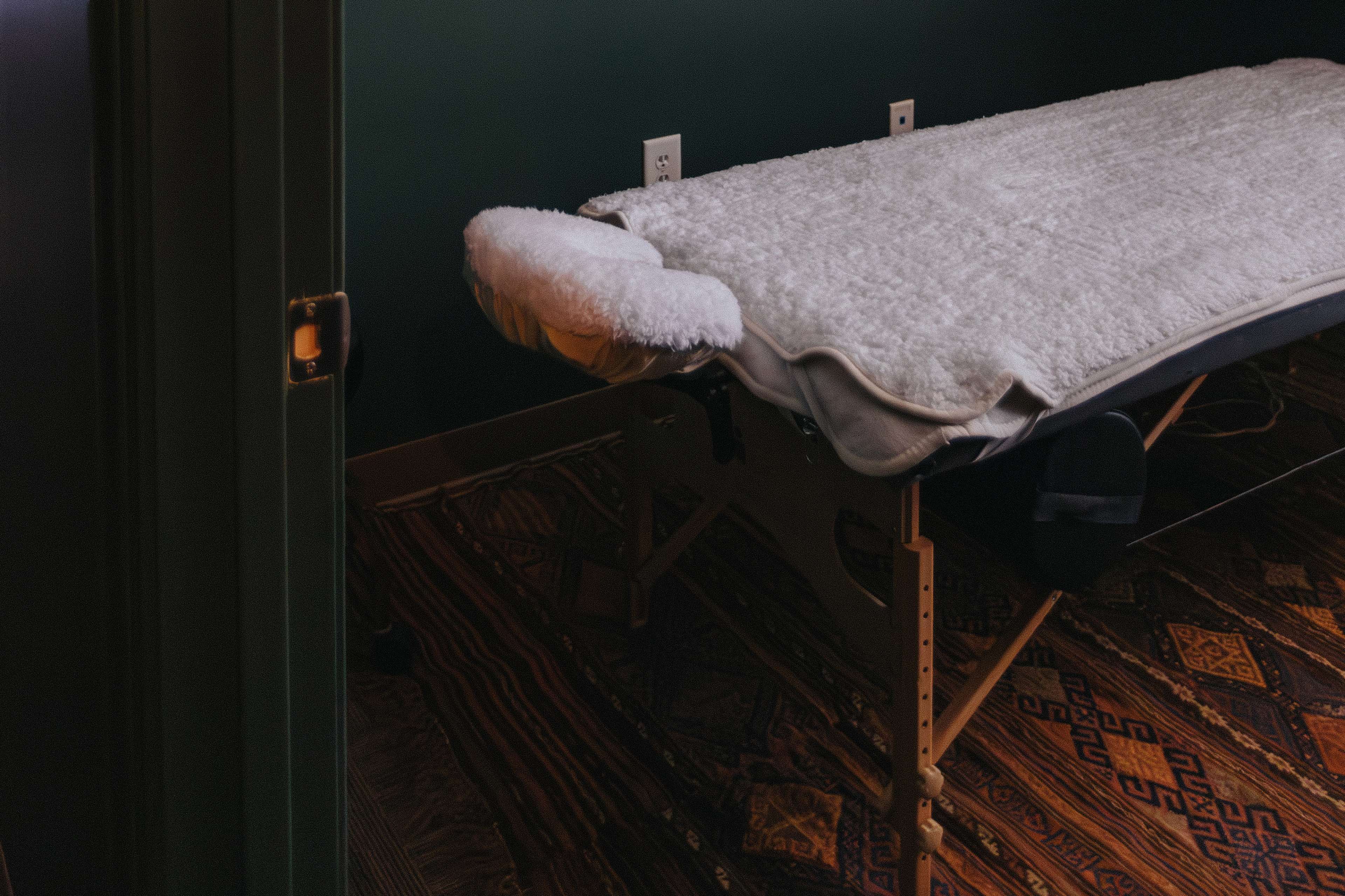 A neatly arranged massage table is positioned against a green wall in a softly lit room.