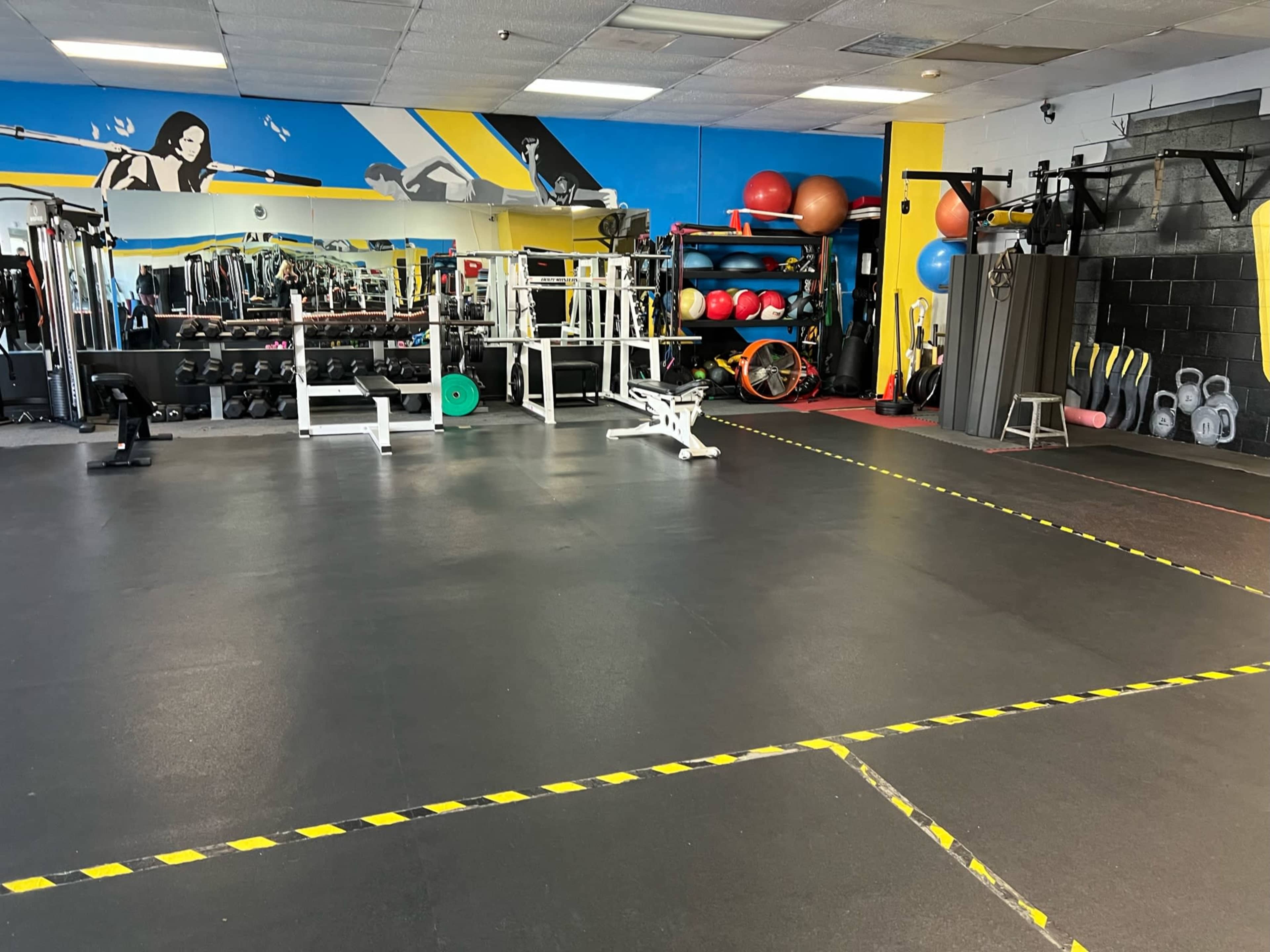 A gym interior with various exercise equipment, including weight benches, dumbbells, and fitness balls, against a colorful mural.